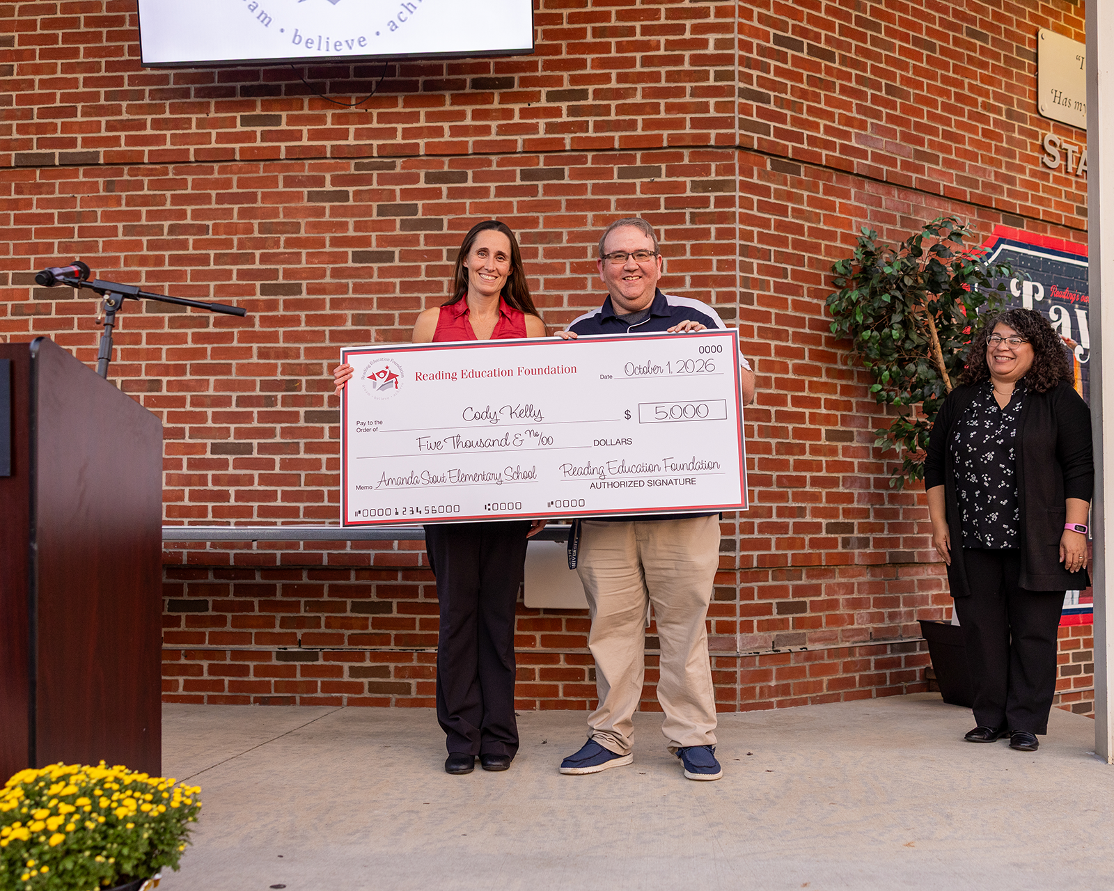 Cody Kelly holding a check from the Reading Education Foundation for his teacher grant in front of a brick background