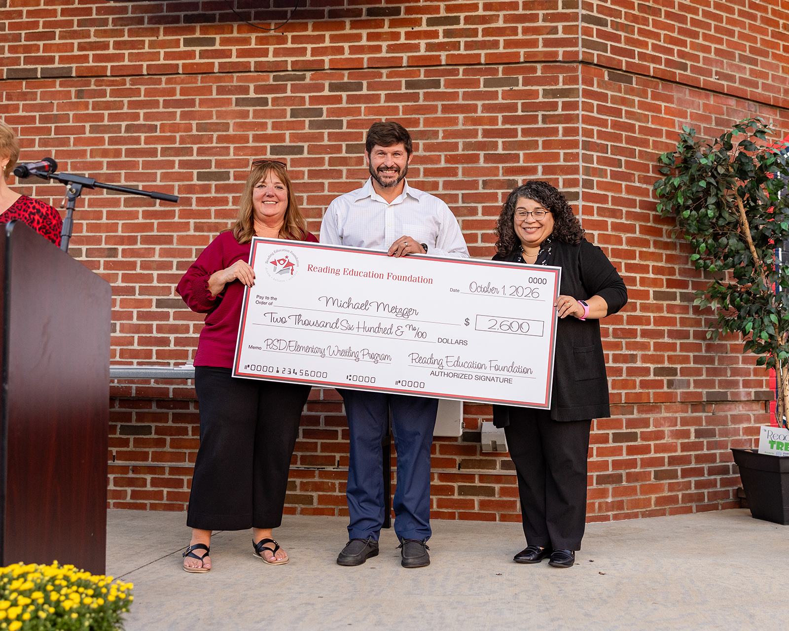 Michael Metzger holding a large check from Reading Education Foundation for his grant in front of a brick wall