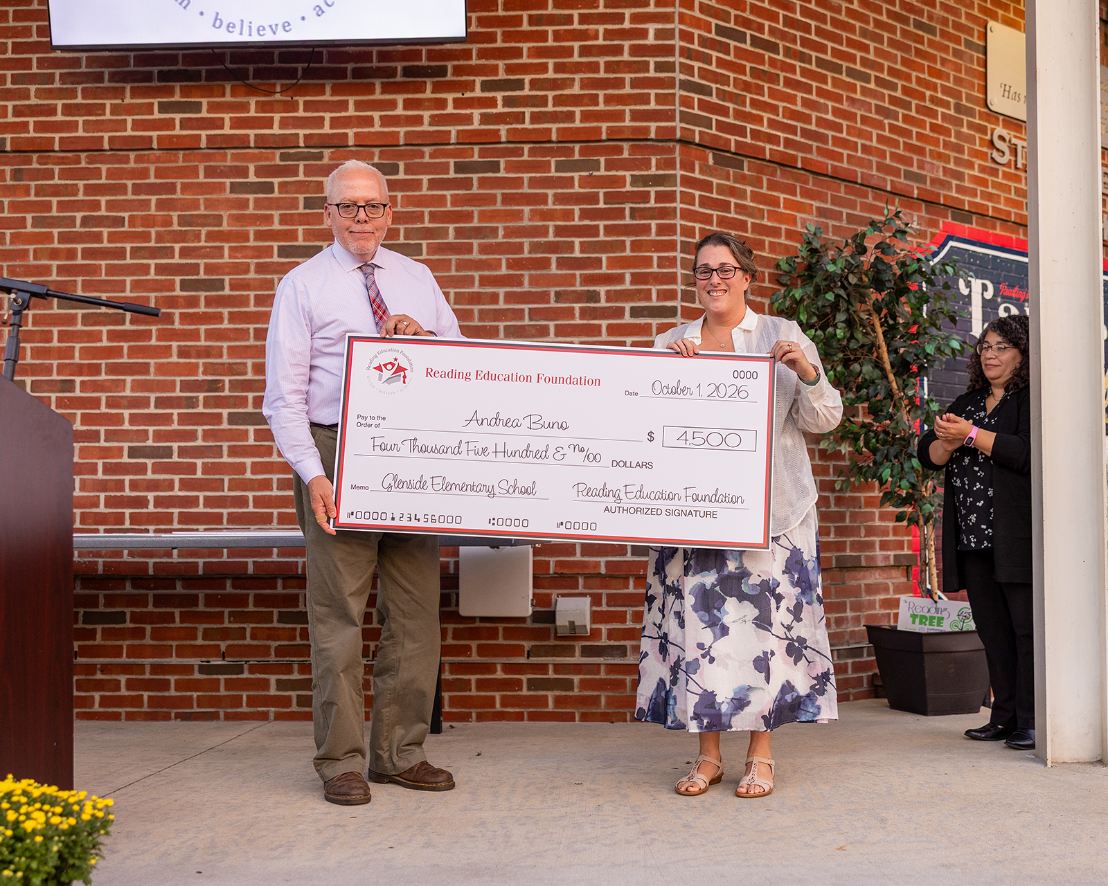 Andrea Buno holding a check from the Reading Education Foundation on a brick background