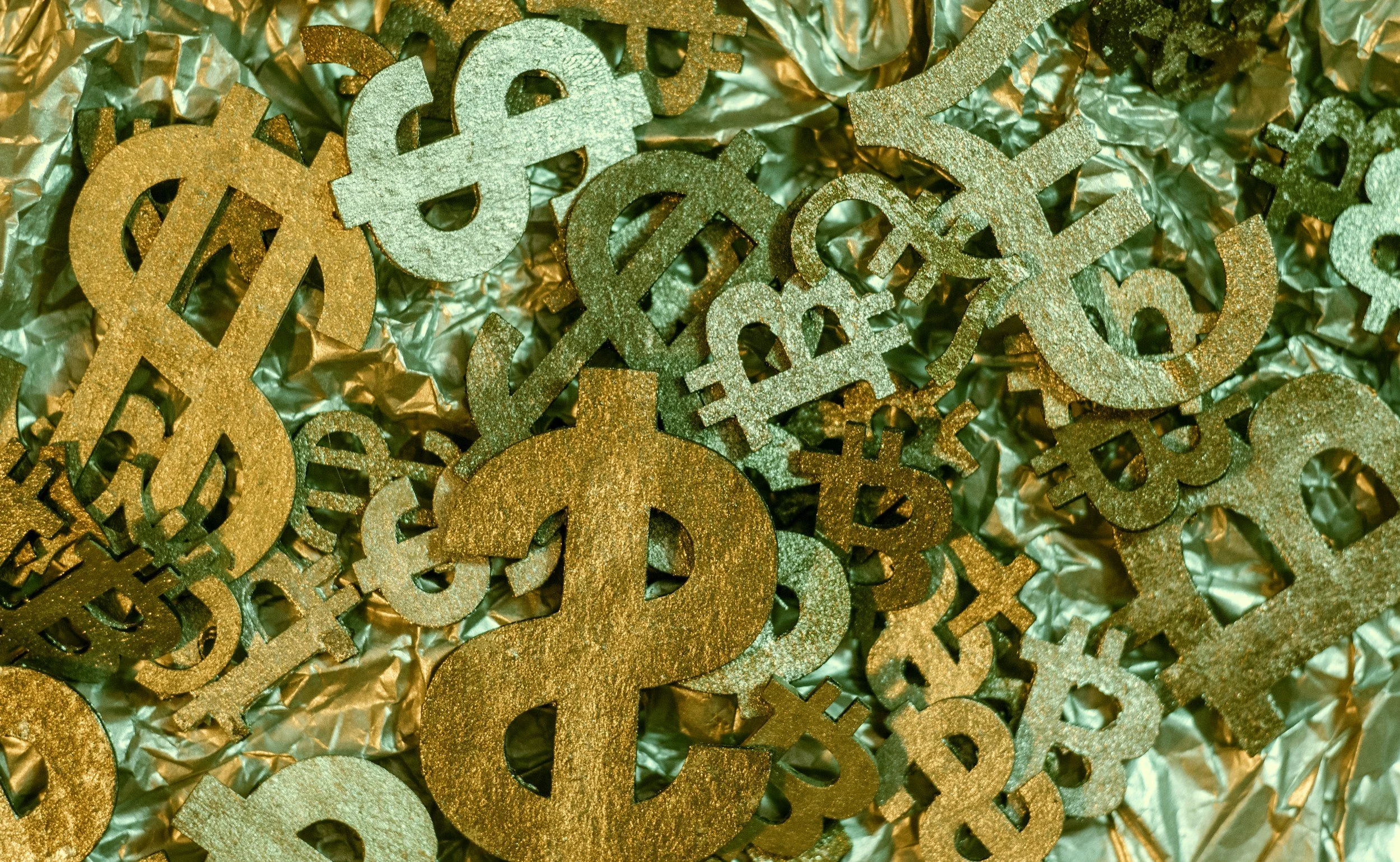 Gold and silver glittered dollar sign decorations on metallic green and gold background.