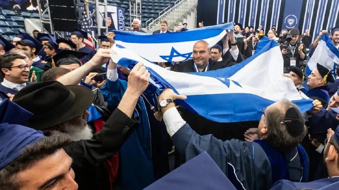 Group of graduates in caps and gowns celebrating at a graduation ceremony, holding and waving Israeli flags.