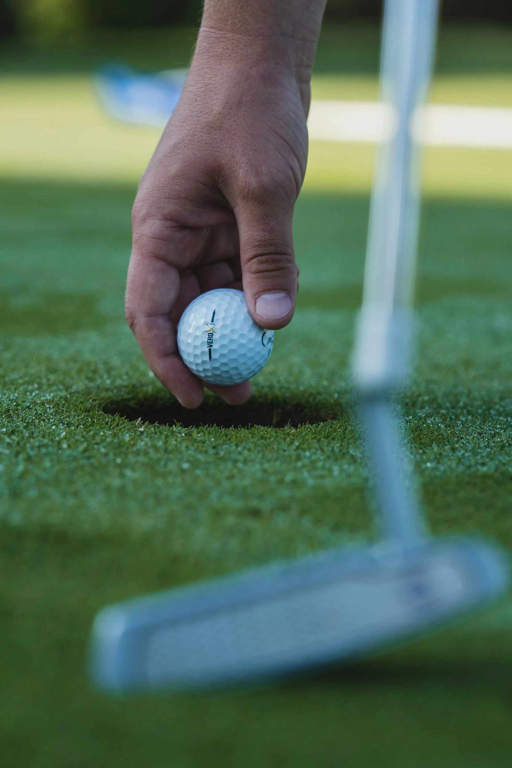 Close-up of a hand placing a golf ball on the grass near a golf hole and flagstick on a putting green
