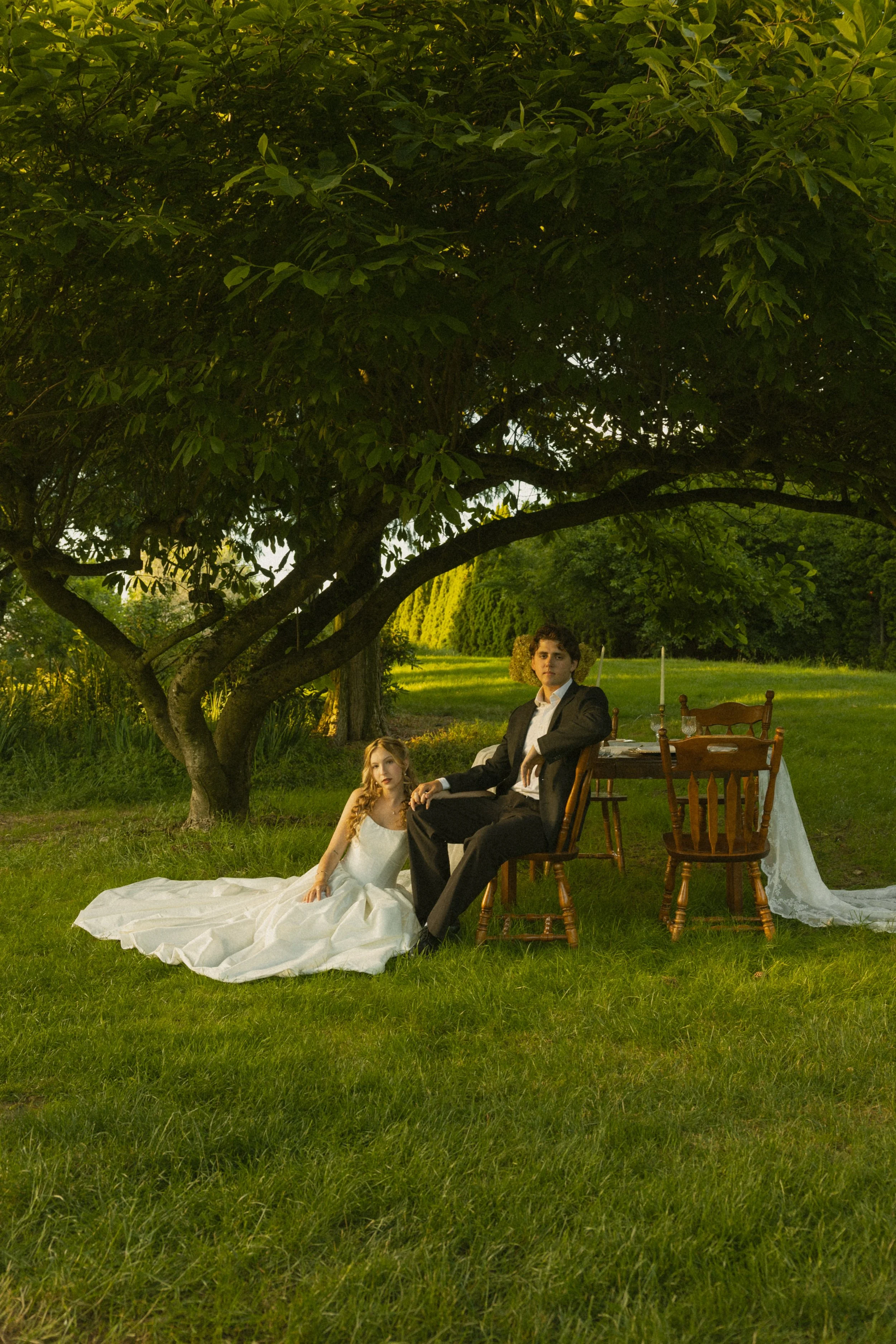 A couple sharing a joyful moment outdoors, with the woman smiling as the man gently holds her face, surrounded by greenery and warm sunlight.
