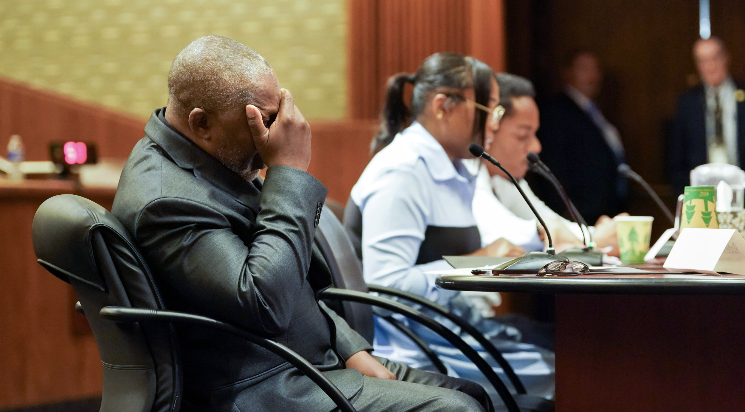 Man in a courtroom covering his face with his hands