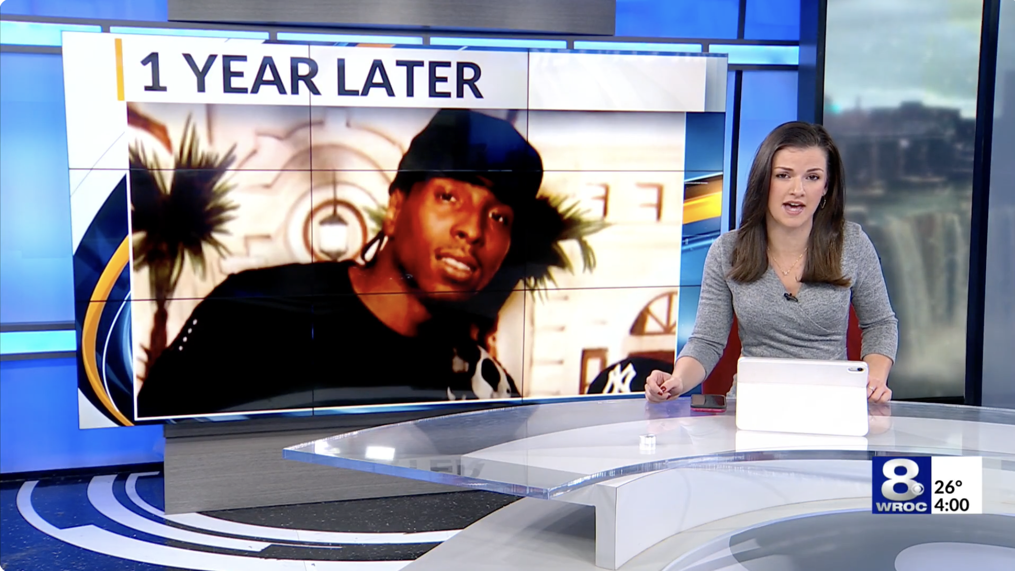 newscaster in front of photo reading 1 year later