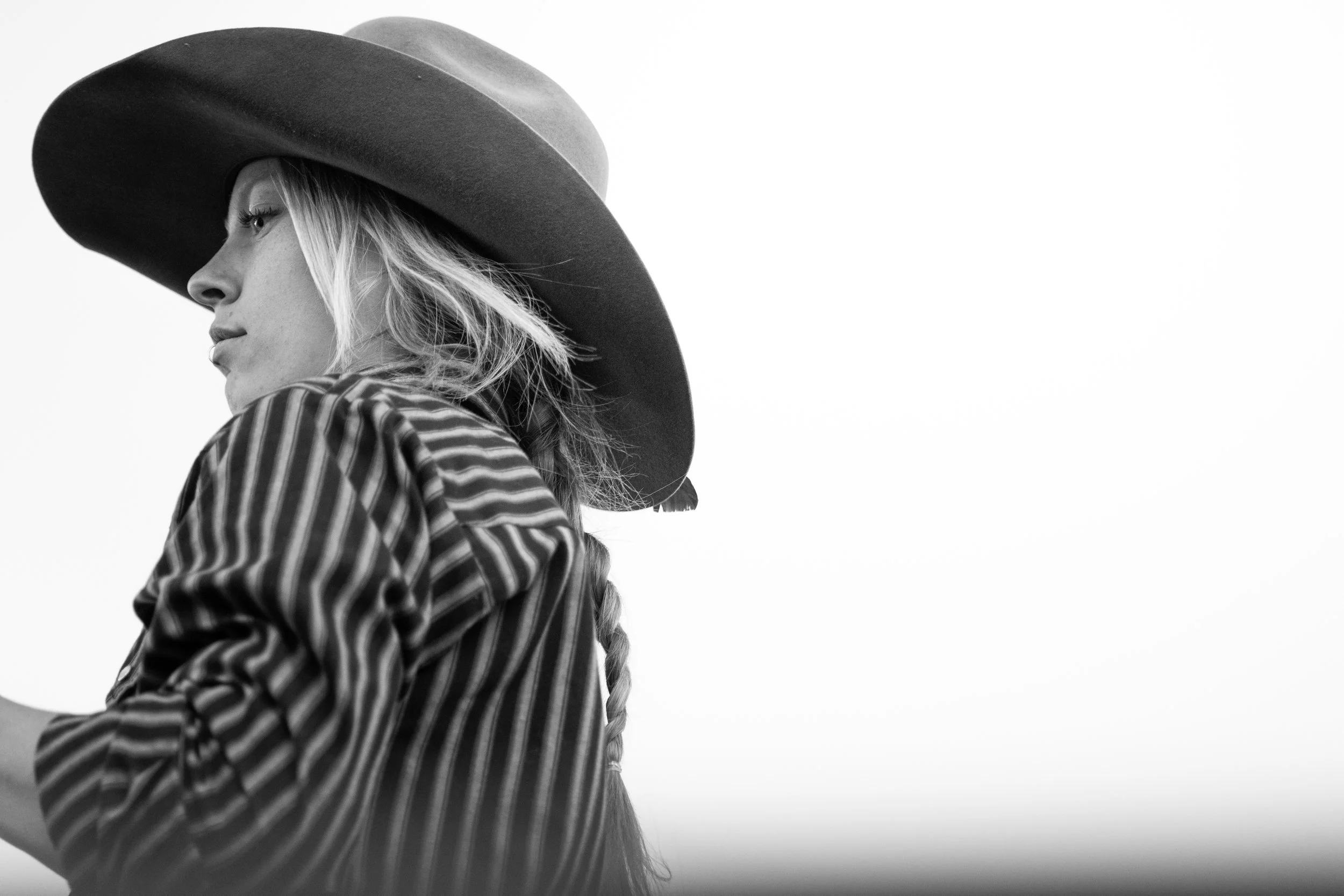 Black and white photo of a woman wearing a wide-brimmed hat and a striped shirt, with her face in profile and long hair in a braid.