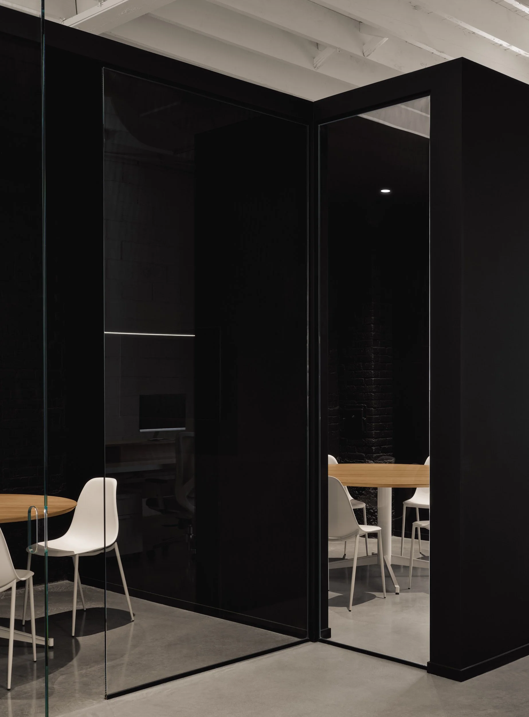 Salle de réunion moderne avec murs noirs, verre et chaises blanches autour d'une table en bois.