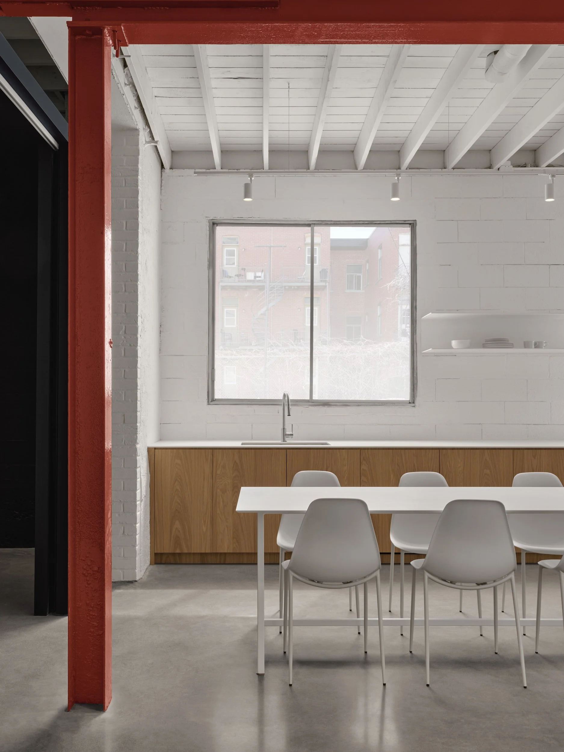 Cuisine moderne avec un grand plan de travail en bois, une fenêtre, une table blanche et des chaises blanches. Le plafond est en bois peint en blanc avec des poutres apparentes.