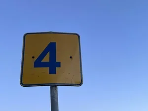 A yellow road sign with the number 4 in black, mounted on a metal pole against a clear blue sky.