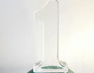 A clear glass trophy in the shape of the number one, placed on a dark surface against a plain light background.