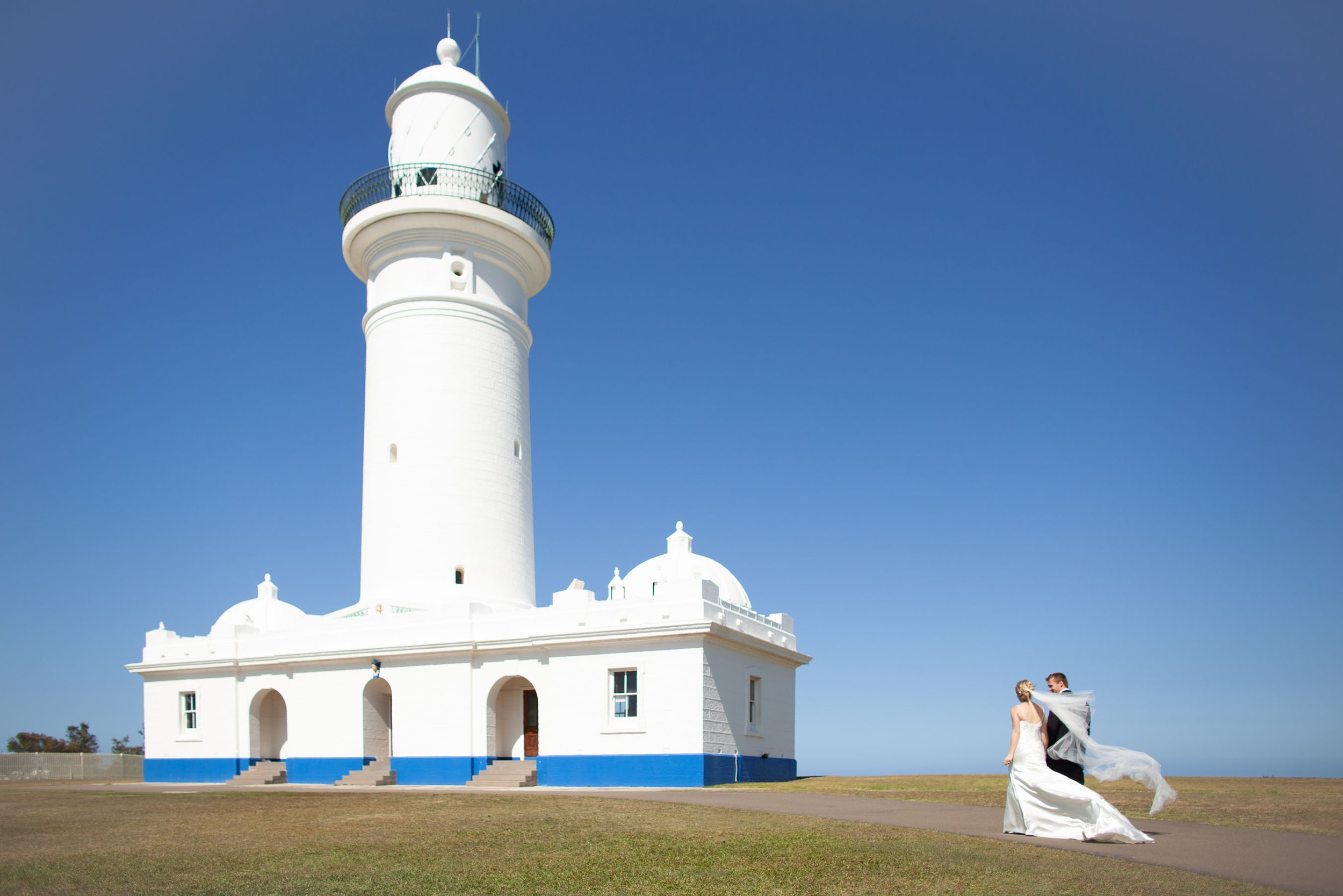 Naomi & Justin walking with a flowing veil towards Macquarie lighthouse at wedding portraits in Vaucluse