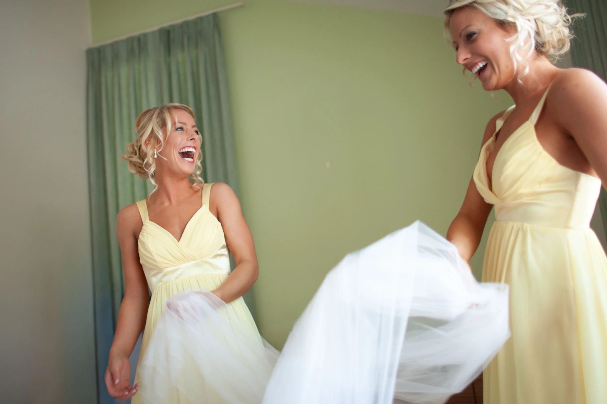 Bridesmaid sisters laughing and playing with bridal veil