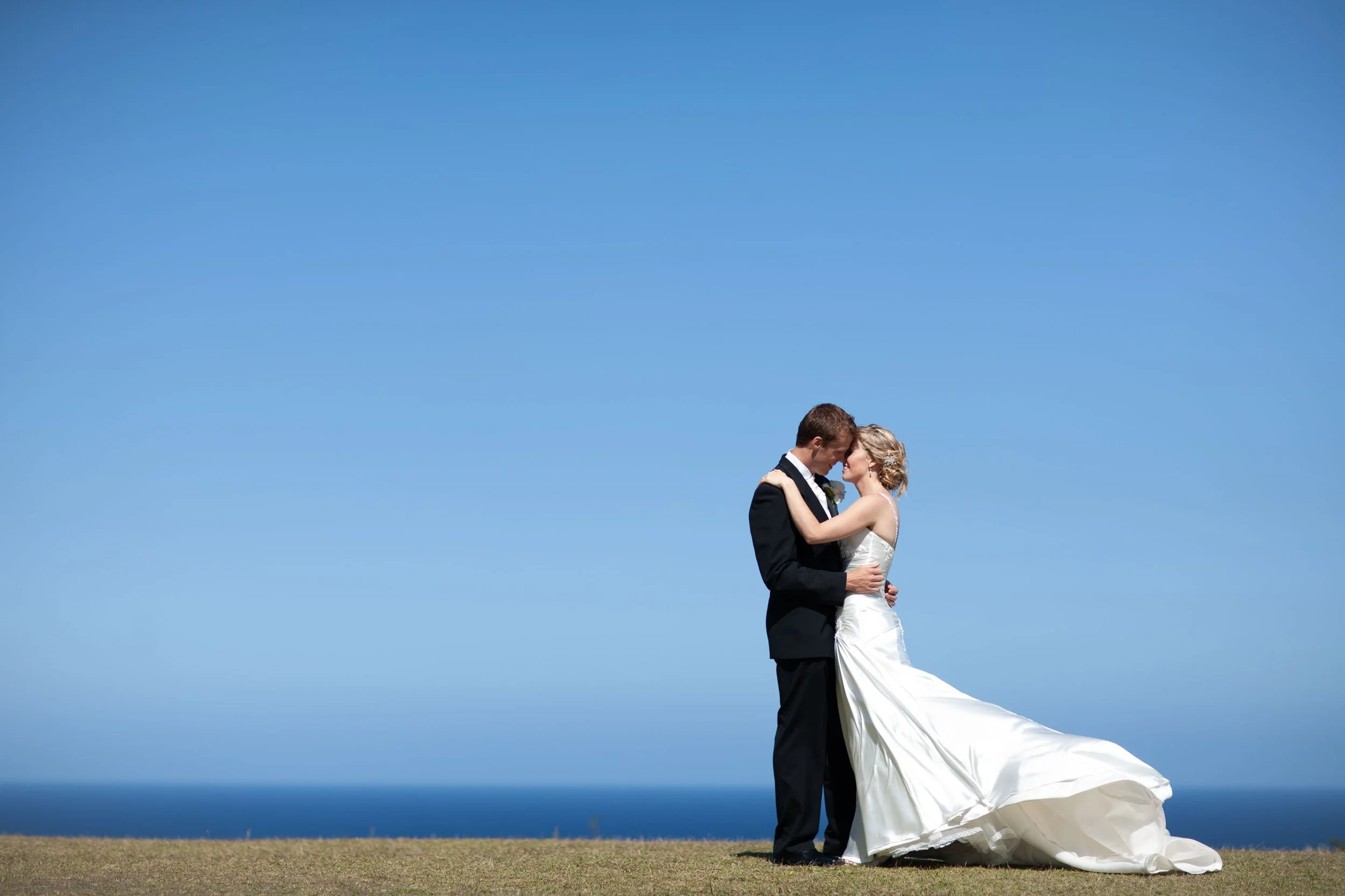 Naomi and Justin wedding portraits embracing under a clear summer sky in Vaucluse Sydney.