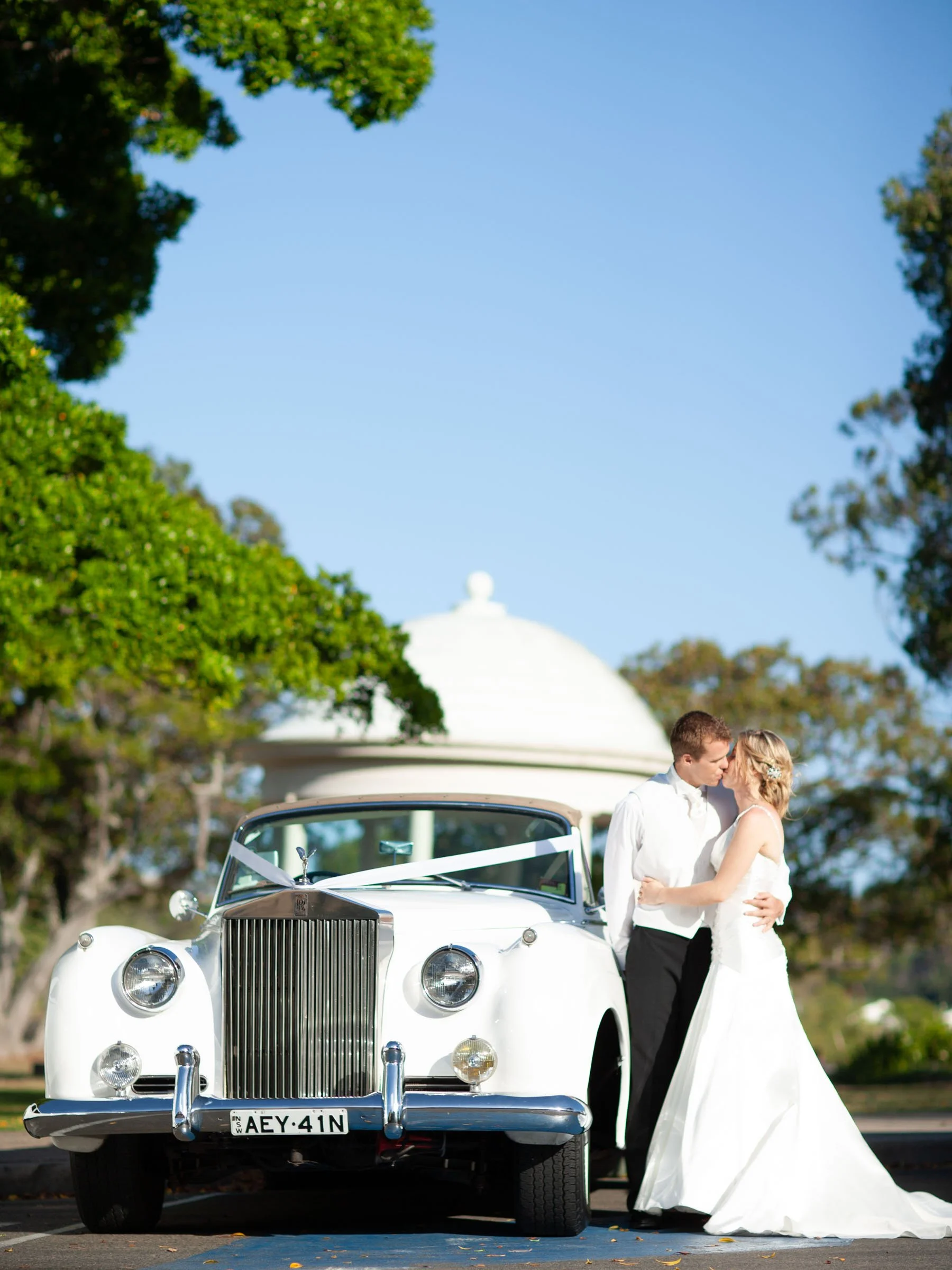 Bride and Groom kiss alongside their Rolls Royce outside Bathers Pavilion at Balmoral Beach