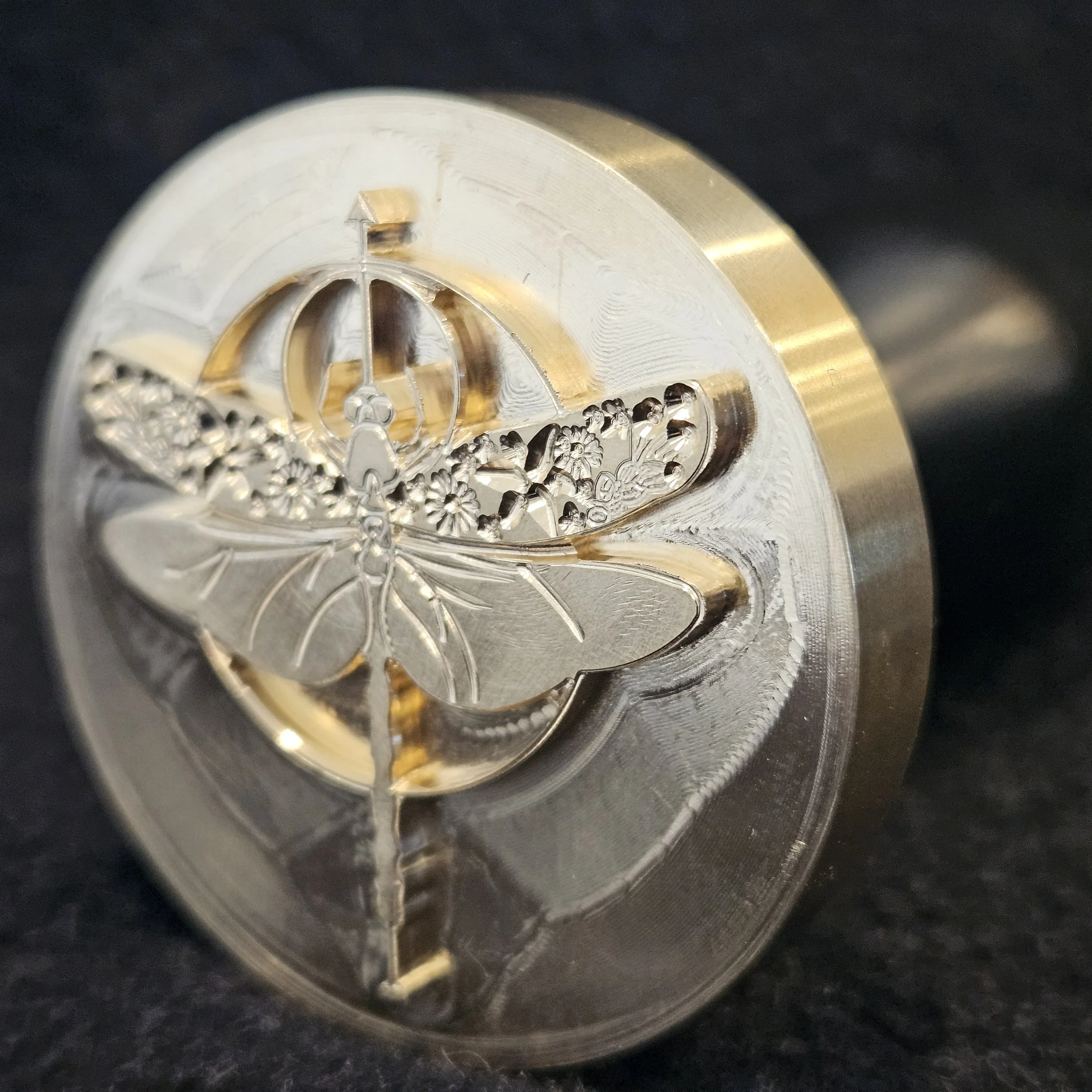 Close-up of a shiny metallic filament bulb, with an intricate design including a butterfly emblem and decorative elements, set against a dark background.