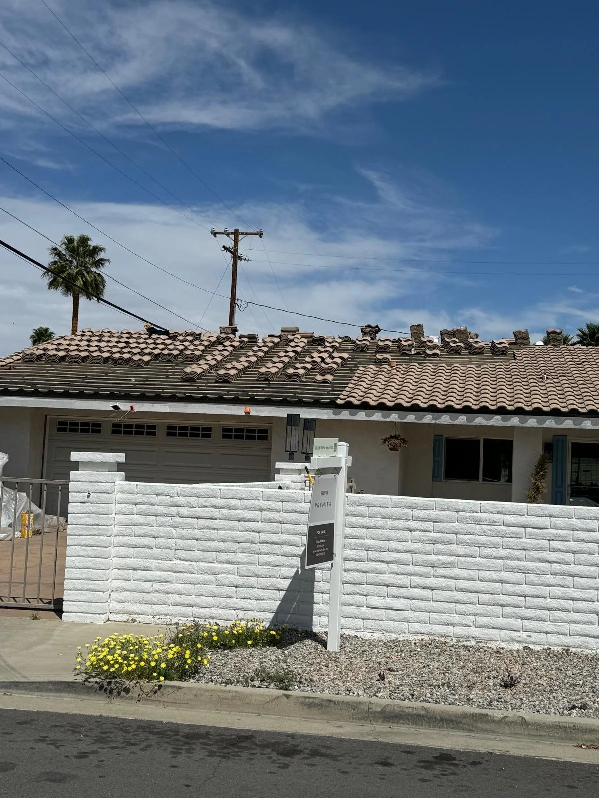 White brick house with a tiled roof, front yard with yellow flowers, and a white mailbox, under a blue sky with some clouds.