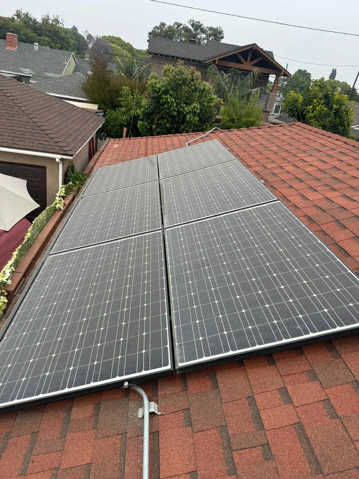 Solar panels installed on a red shingled rooftop, with neighboring houses and trees in the background.