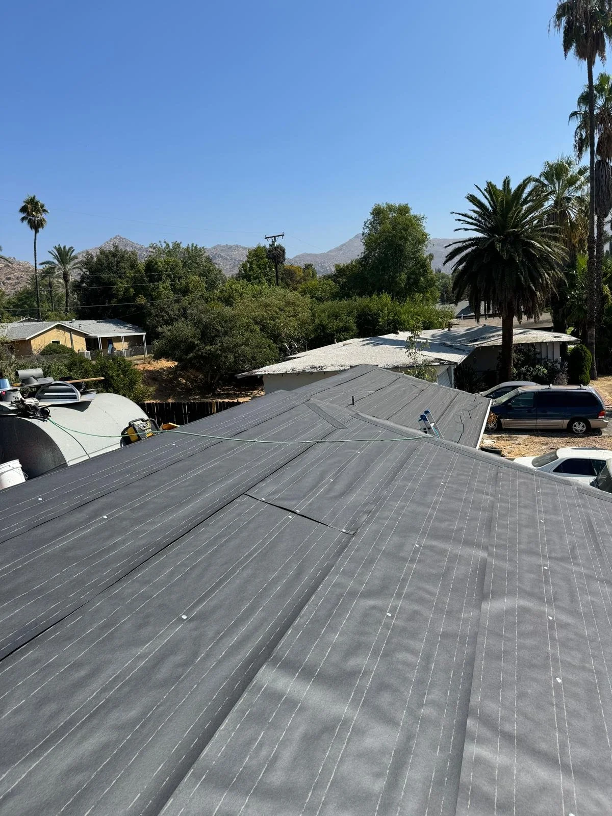 View of rooftops, palm trees, and distant mountains under a clear blue sky.