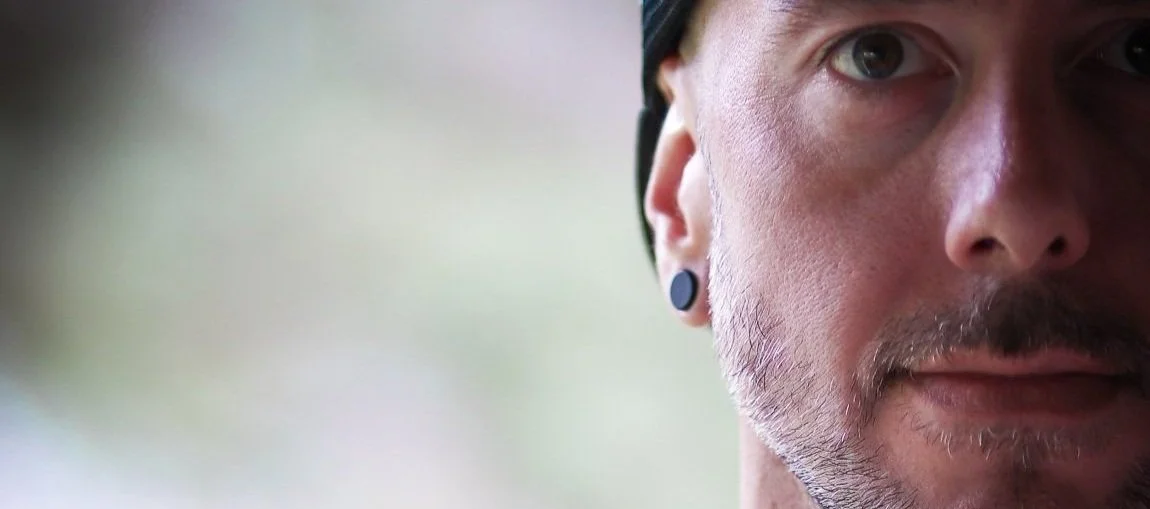 A close-up of a partially visible man's face, showing his eye, nose, and mouth, with a blurred background.