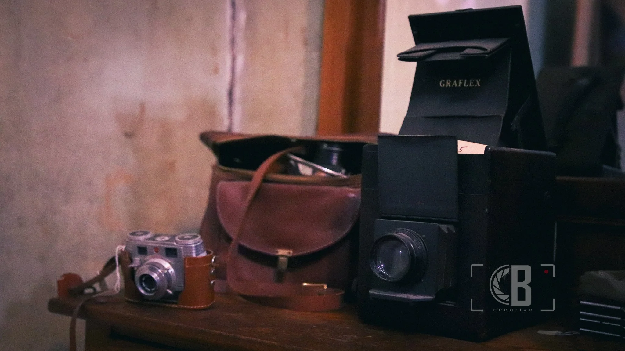 Vintage camera with brown leather case and black vintage camera with a box, all placed on a wooden surface