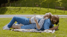 Two children playing on the grass outdoors, one lying down and the other leaning over. They appear to be enjoying sunny weather.