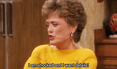 A woman wearing a yellow sweater with short, curly hair speaking and saying, "I am shocked and I want details!"