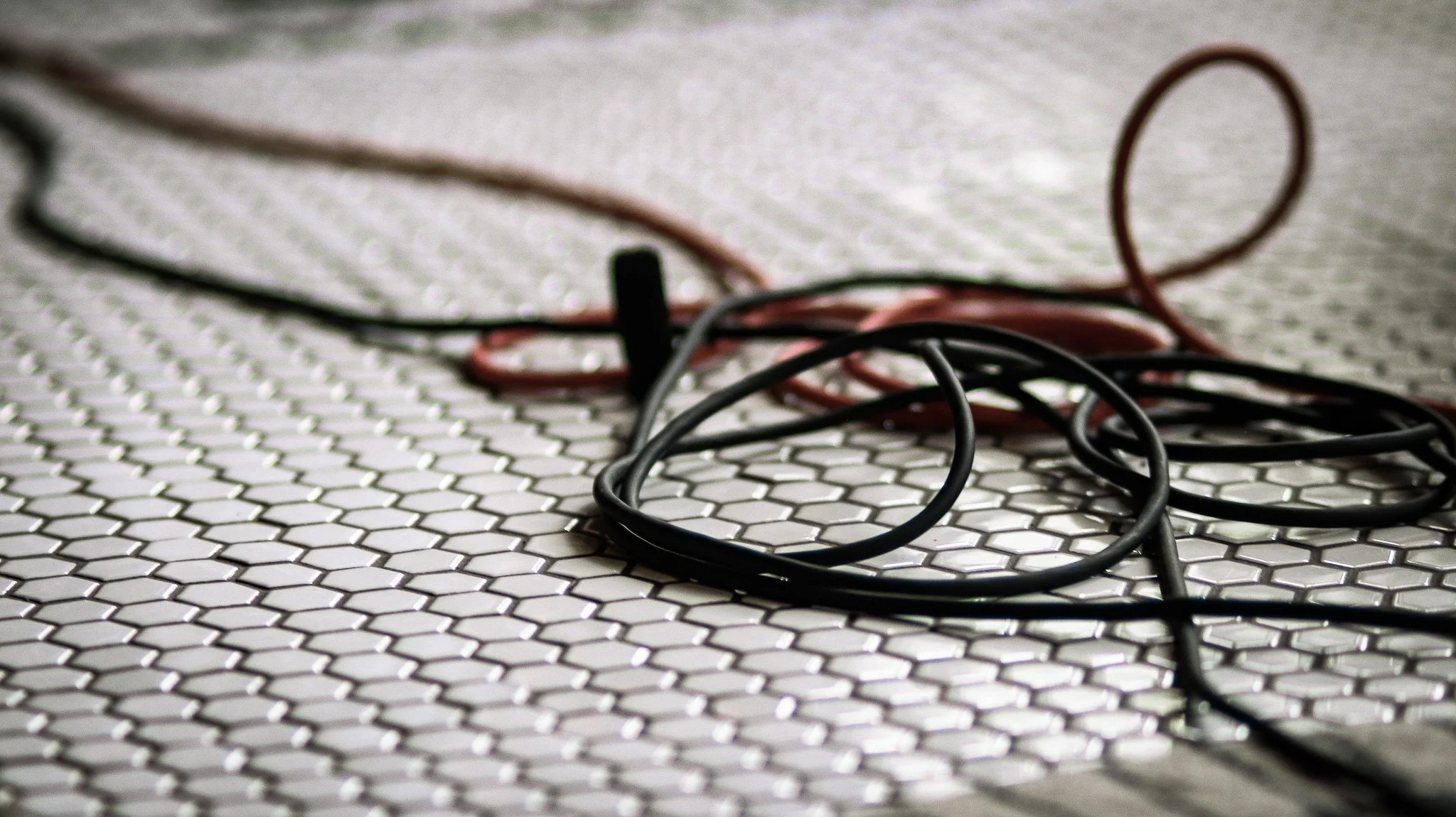 Several tangled black and red electrical cords on a white hexagonal-tile floor.