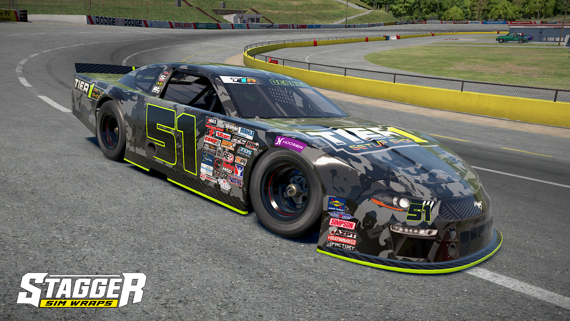 A race car with the number 51, camouflage pattern, and numerous sponsor stickers, on a racetrack with a curve and yellow safety barriers.