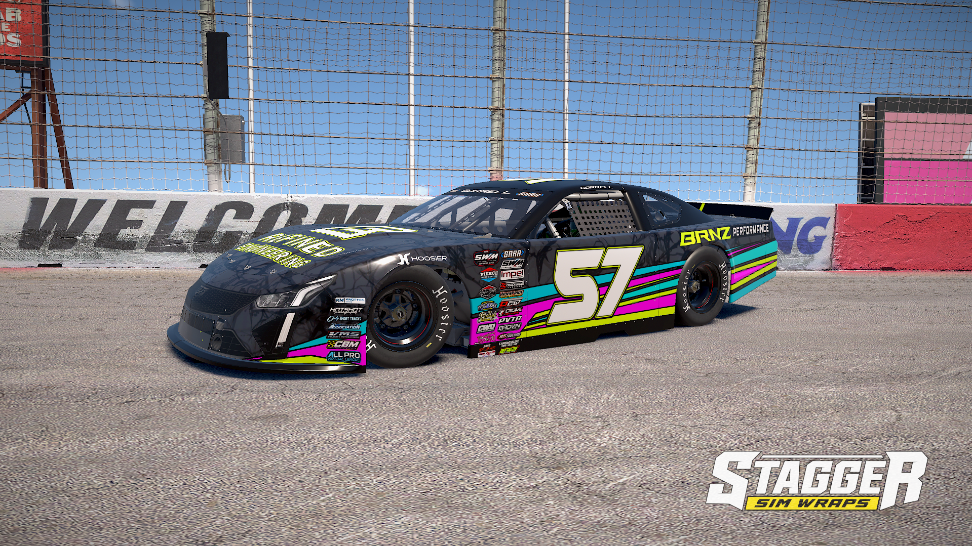A race car with black, pink, blue, and yellow stripes, and the number 57, on a racing track with a red and white wall and a wire fence in the background. The car features various sponsor logos.