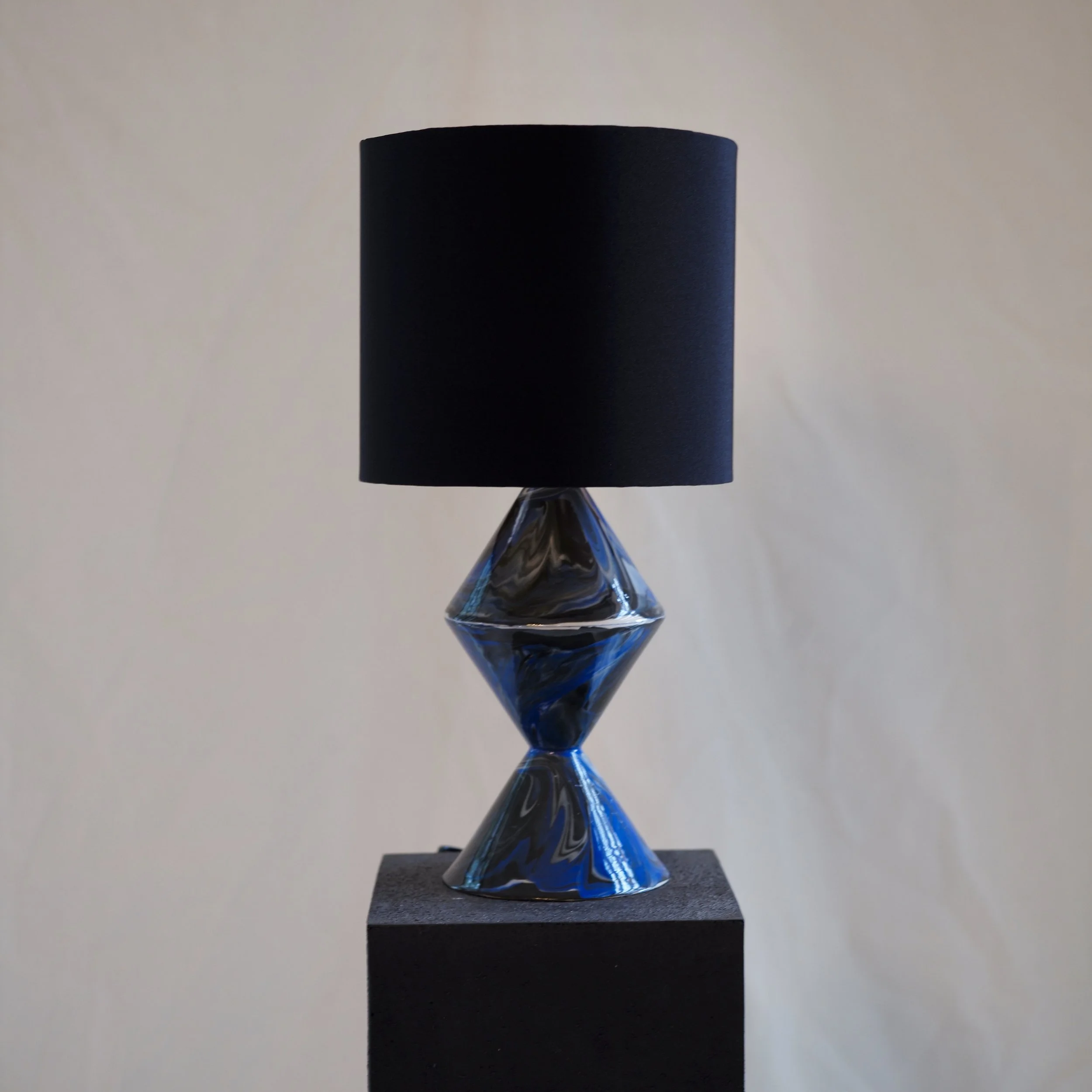 A black cylinder object with a matte finish, placed on a black platform against a plain light background.