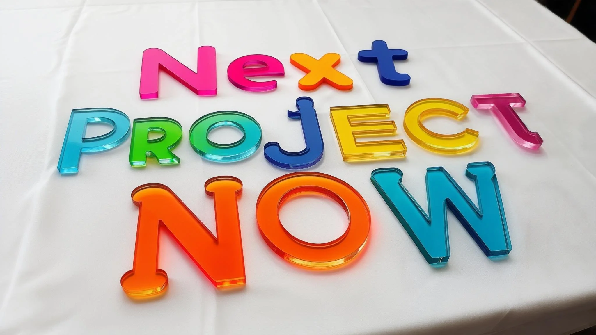 Colorful plastic letters spelling 'Next Project Now' on a white table.
