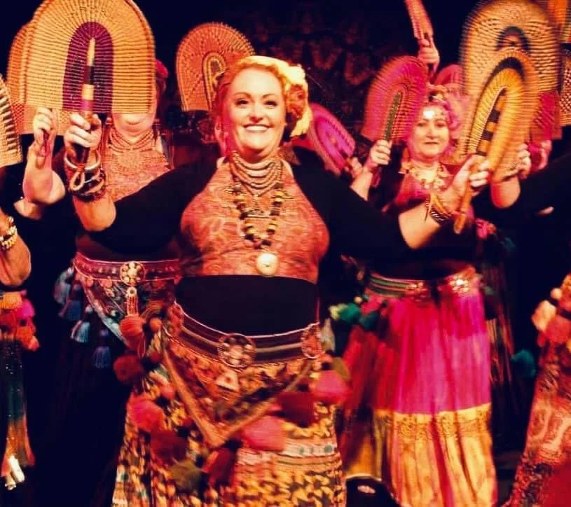 Women dressed in colorful traditional African attire, holding woven baskets, dancing at Bendigo Tribal Festival. Alicia leading the dance.