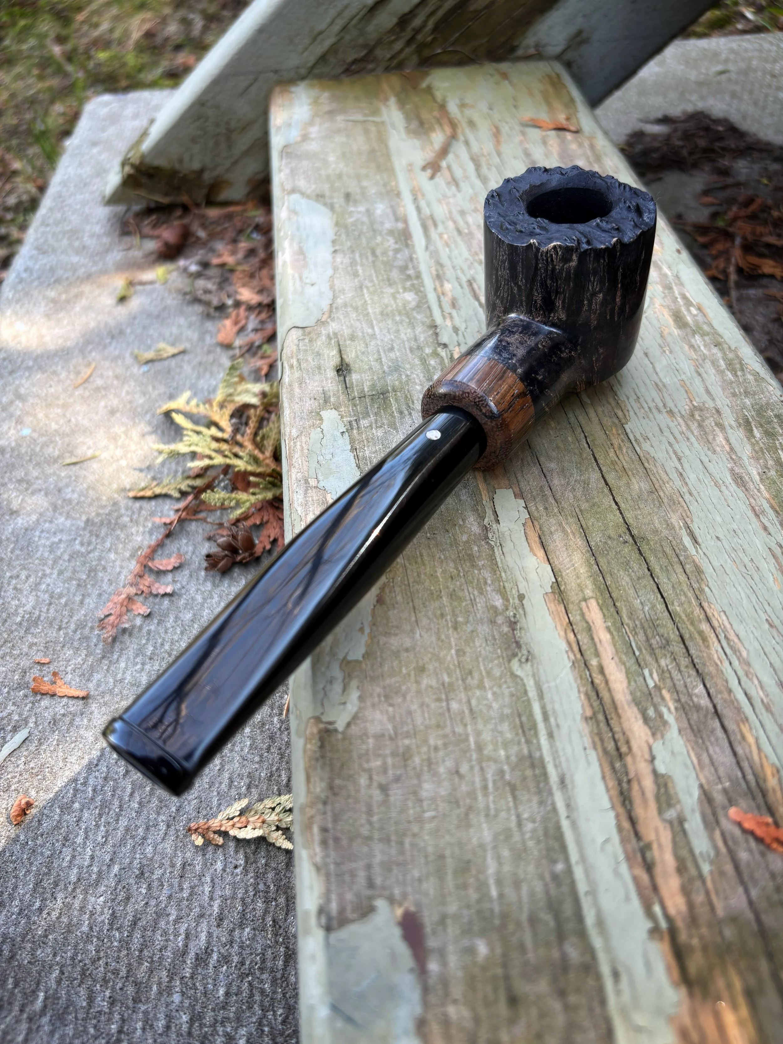 A plateau-pot tobacco smoking pipe resting on a weathered picnic table in an outdoor setting.
