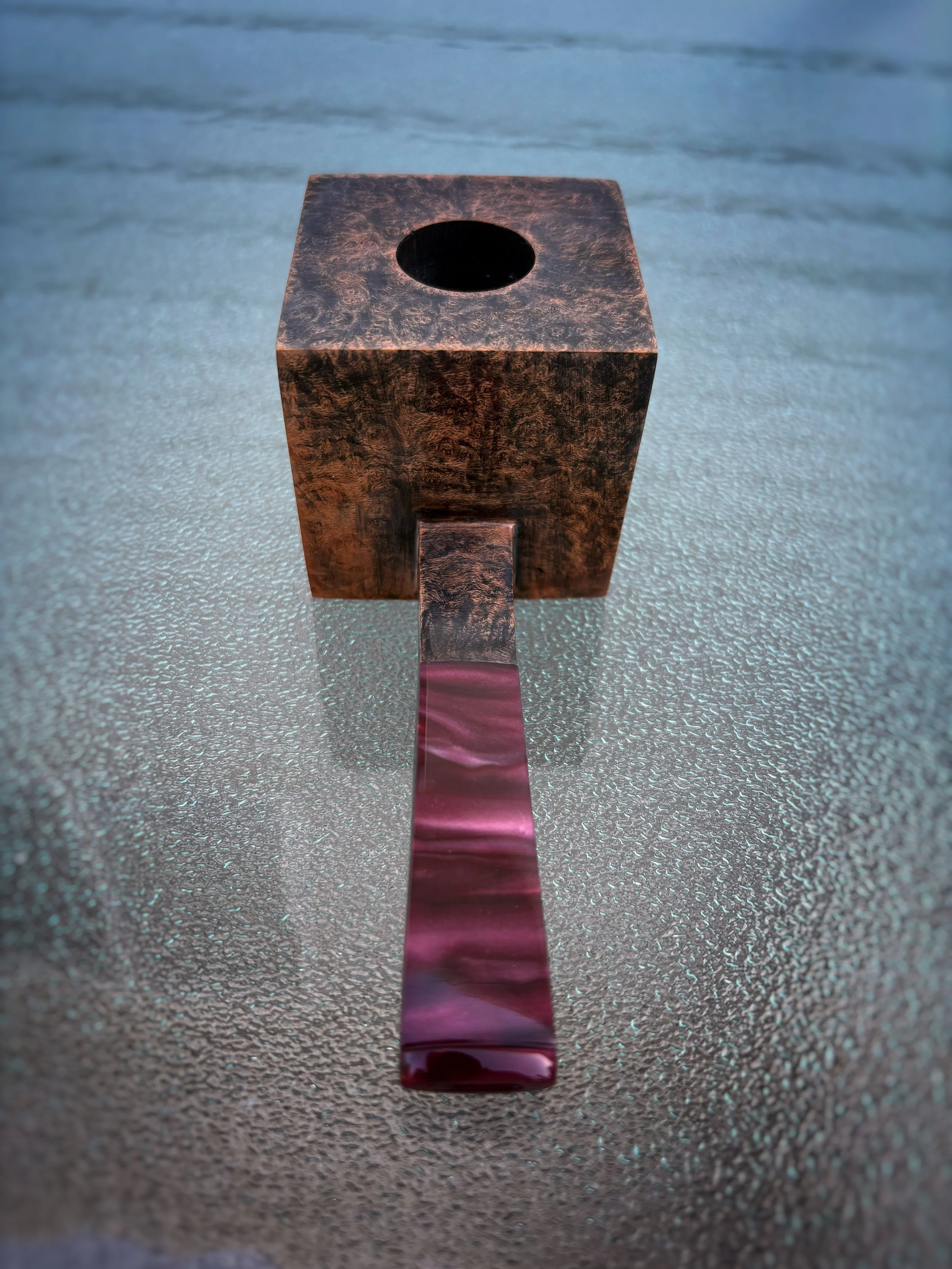 A Cube briar tobacco smoking pipe, positioned on a textured surface.