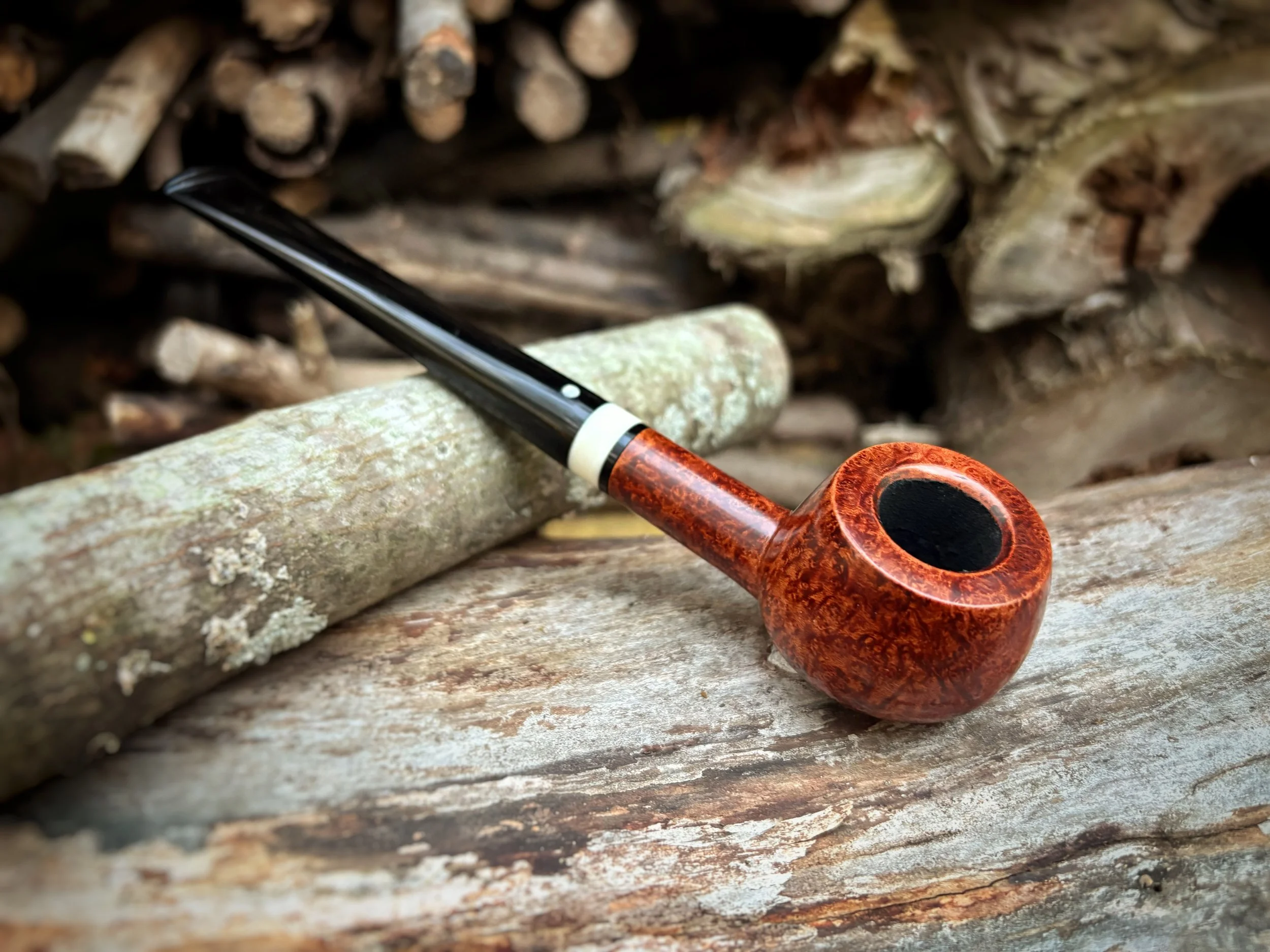 A wooden Prince smoking pipe with a curved stem resting on a weathered logs surface outdoors.