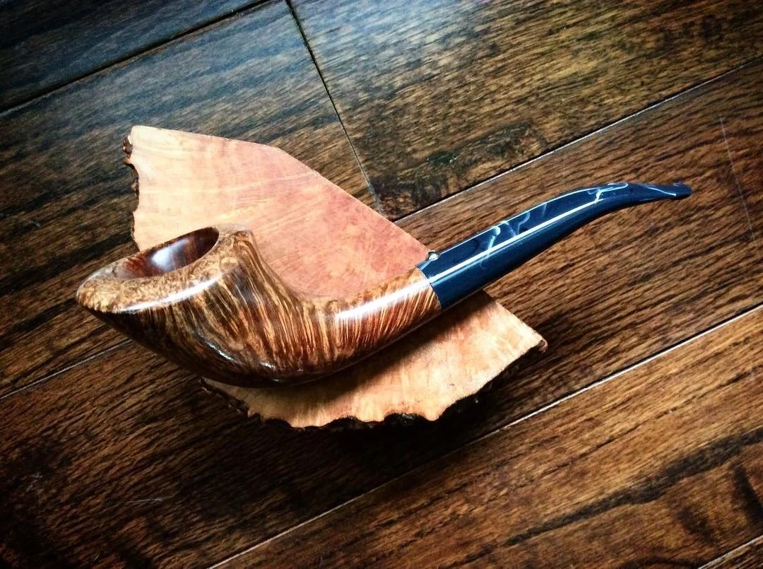 A Horn tobacco pipe with a wooden bowl and a black and brown stem, resting on a wooden surface and a dried leaf.