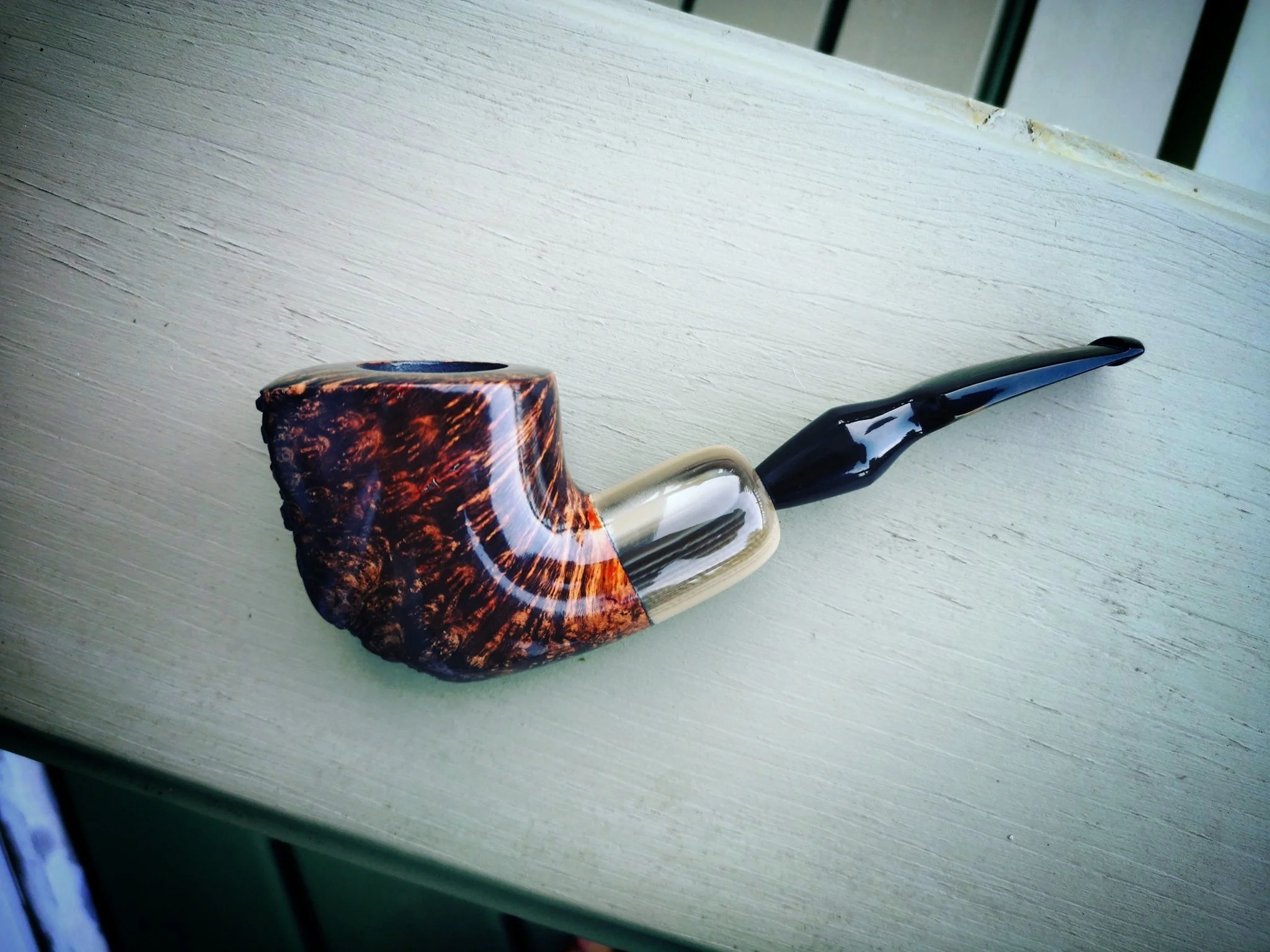 A Freehand smoking pipe with a large, curved, brown and black patterned bowl and a black stem, resting on a light-colored wooden surface.