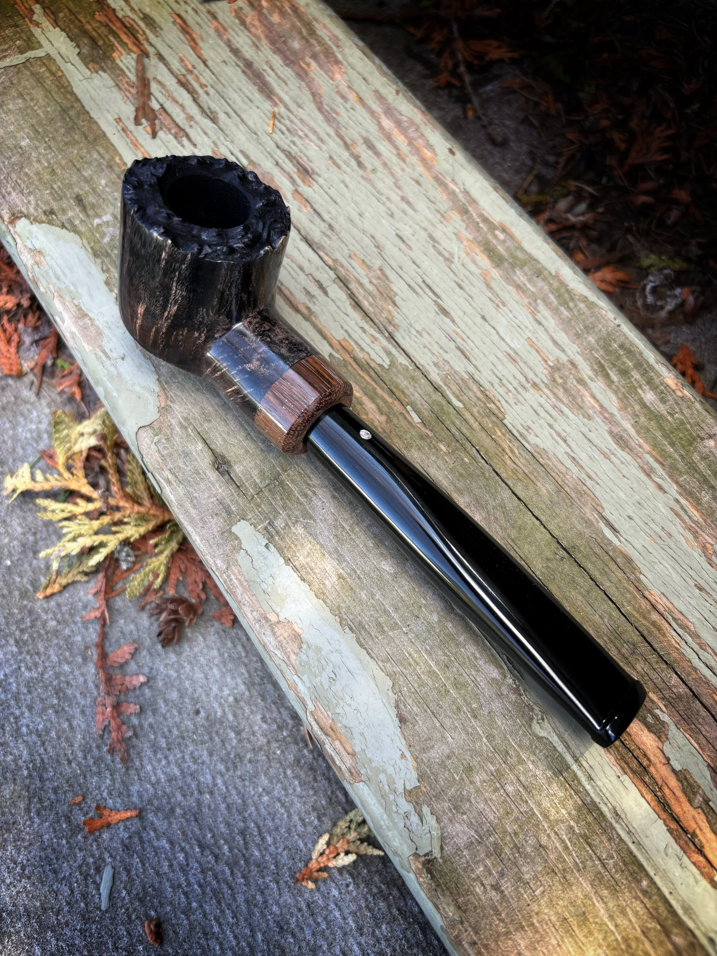 A Plateau-pot tobacco smoking pipe with a wooden bowl and a black stem resting on a weathered wooden bench outdoors.