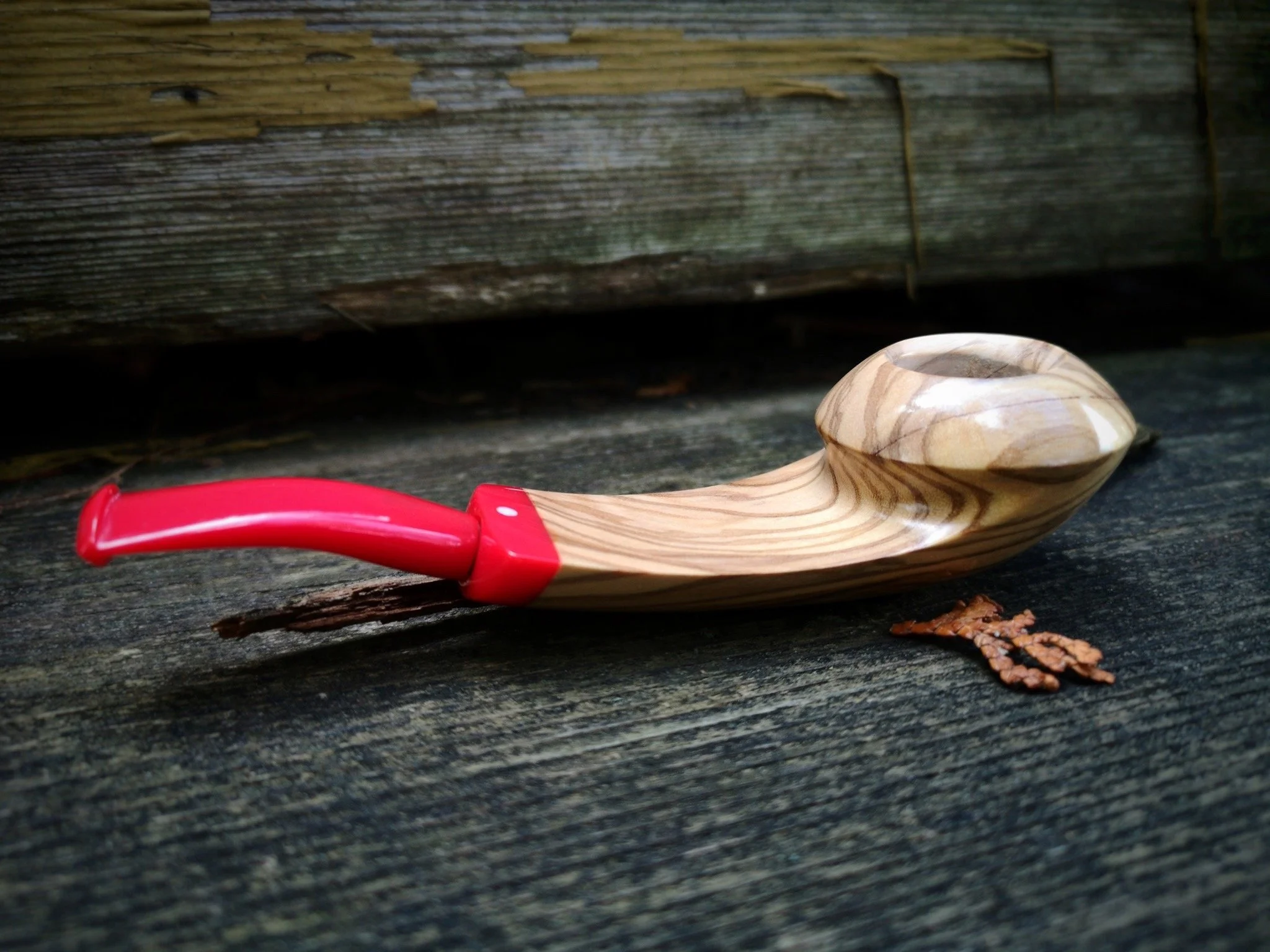 A Wooden Eskimo pipe with a red mouthpiece lying on a weathered wooden surface.