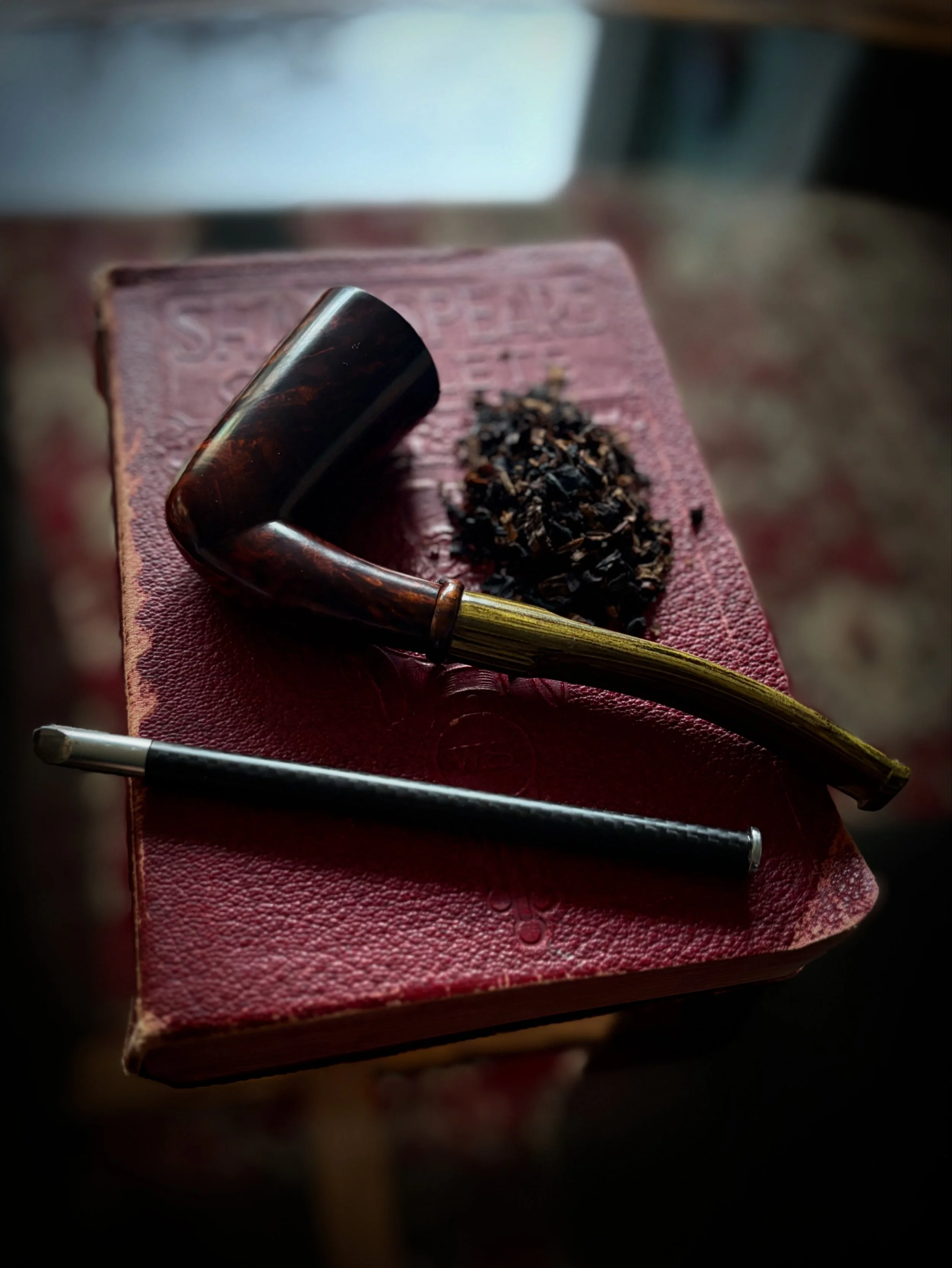 A red book with a pipe, loose tobacco, and a pipe tamper on top.