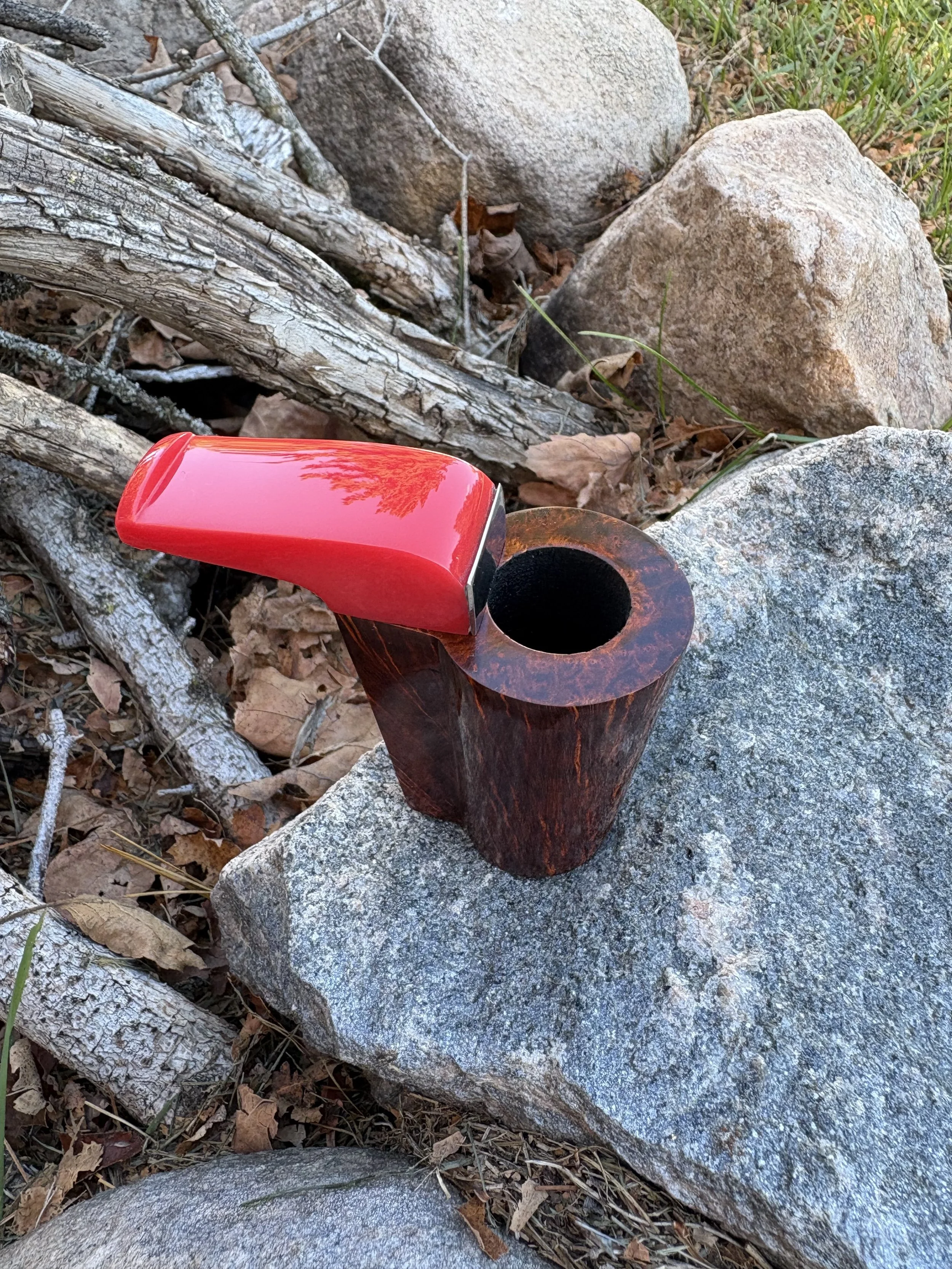 A wooden pocket pipe, placed on a large stone outdoors. The ashtray has a red telephone handset resting on its rim, with trees and rocks in the background.