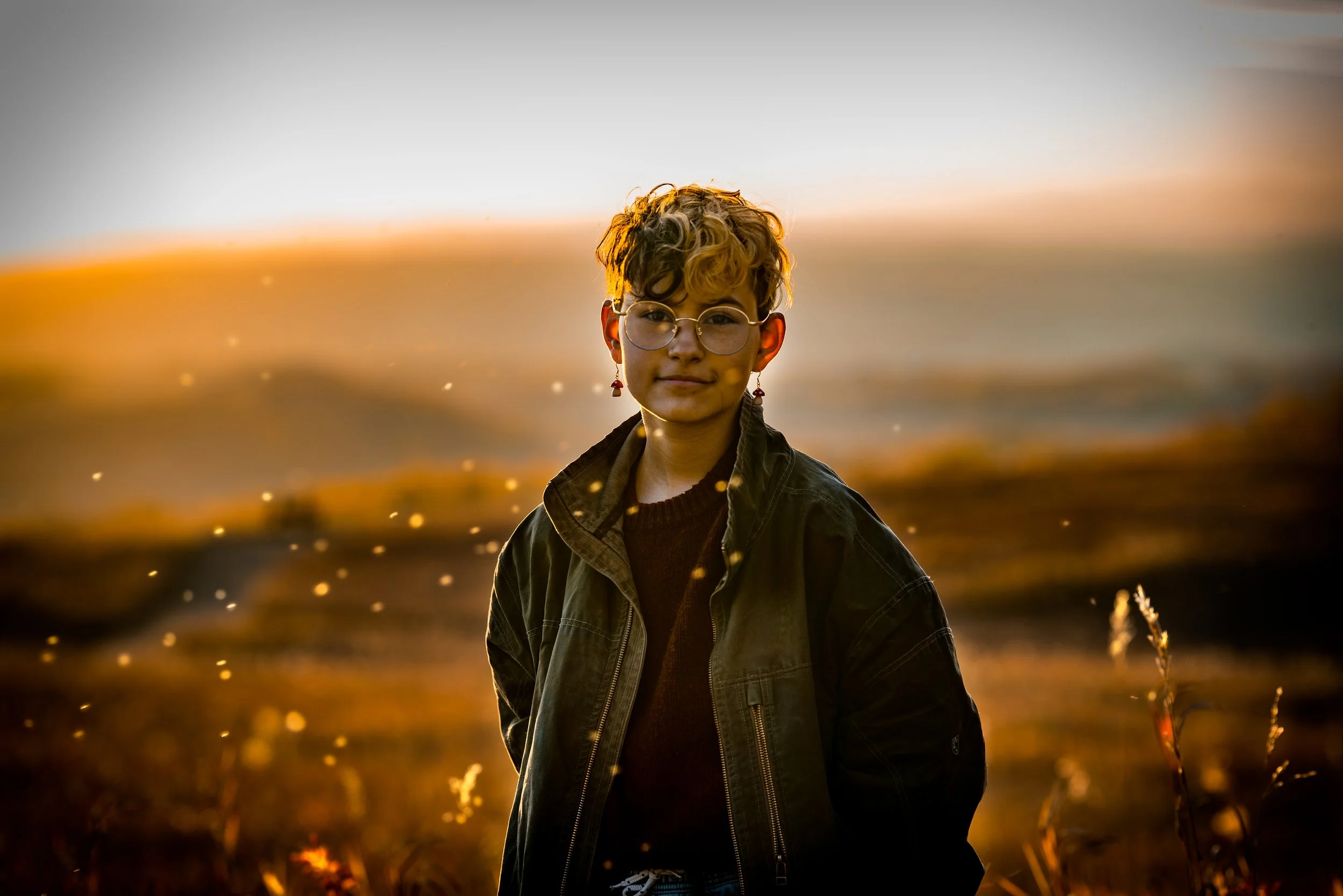 Fine-art portrait of a person in a sunlit field at golden hour, with soft haze and glowing highlights adding depth and mood.