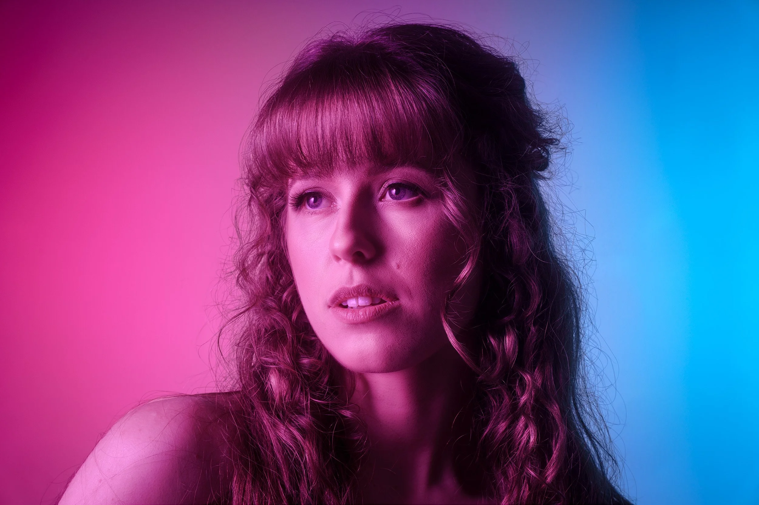 This cinematic fine art portrait explores controlled gradient lighting, where soft magenta tones wrap around the subject and fall into sculpted shadow. The minimalist composition emphasizes form, mood, and presence—hallmarks of TBStudios’ editorial p