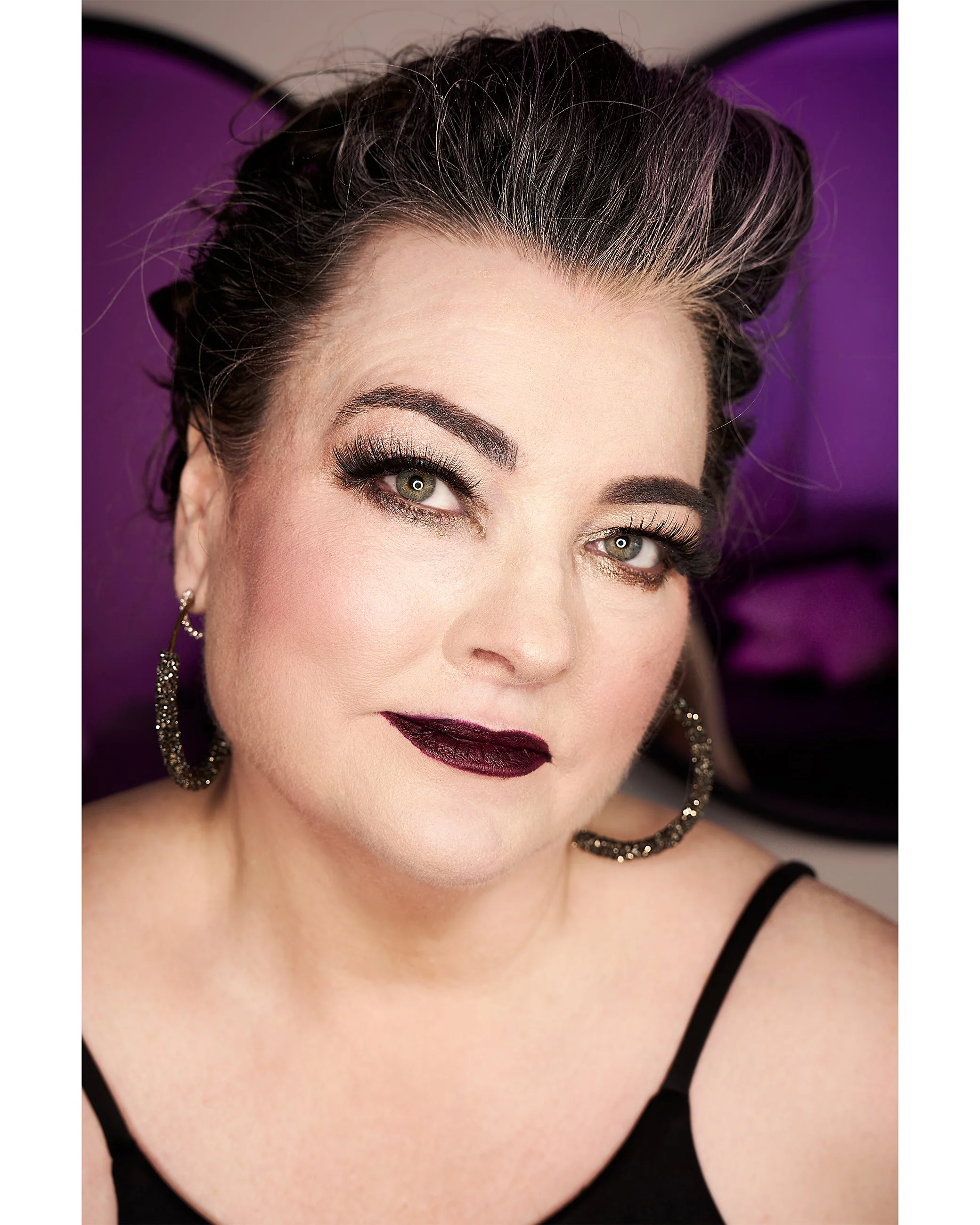 Editorial-style studio portrait with dramatic makeup and purple background lighting.
