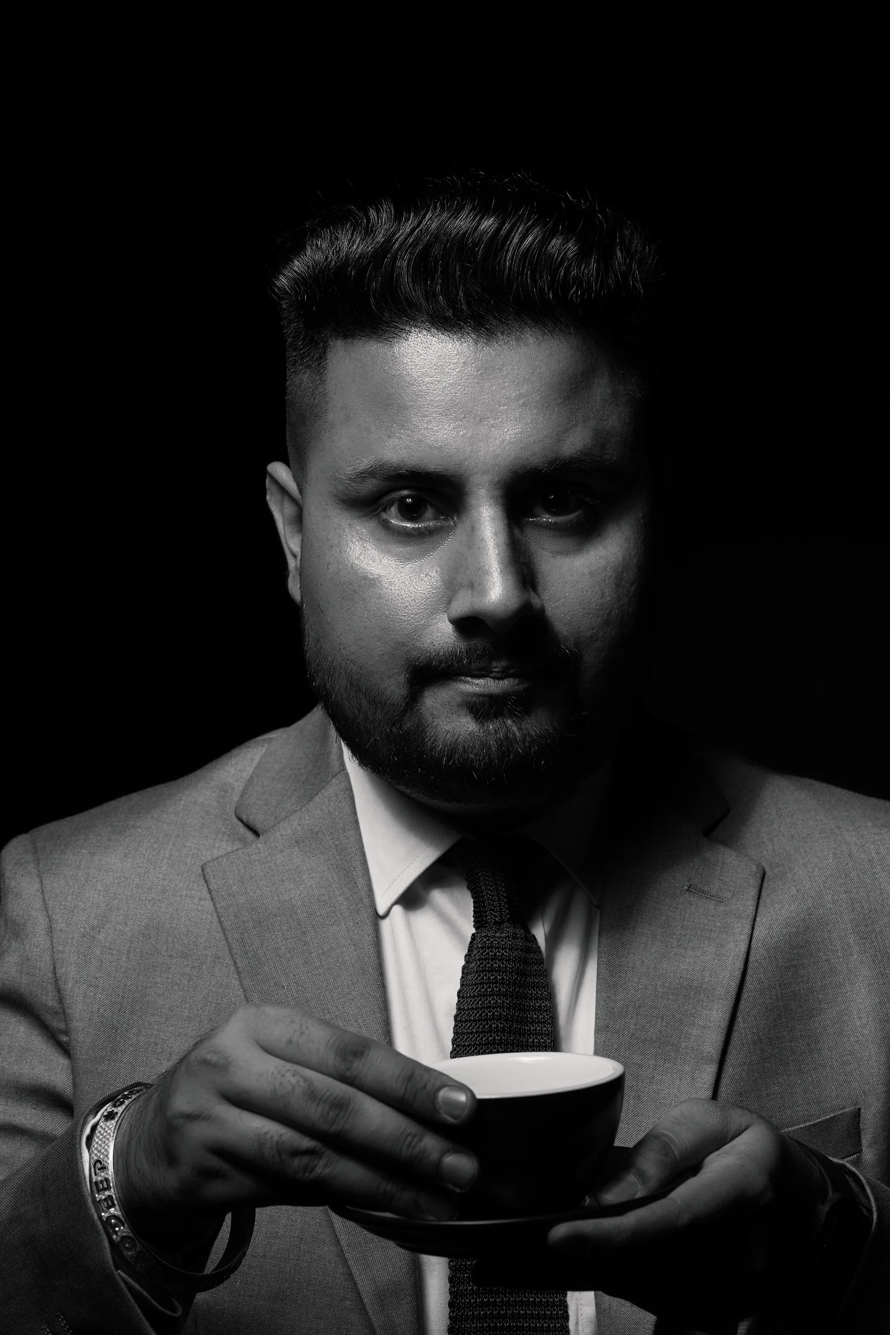 Professional black-and-white portrait of a man in a suit holding an espresso cup, conveying confidence and quiet intensity