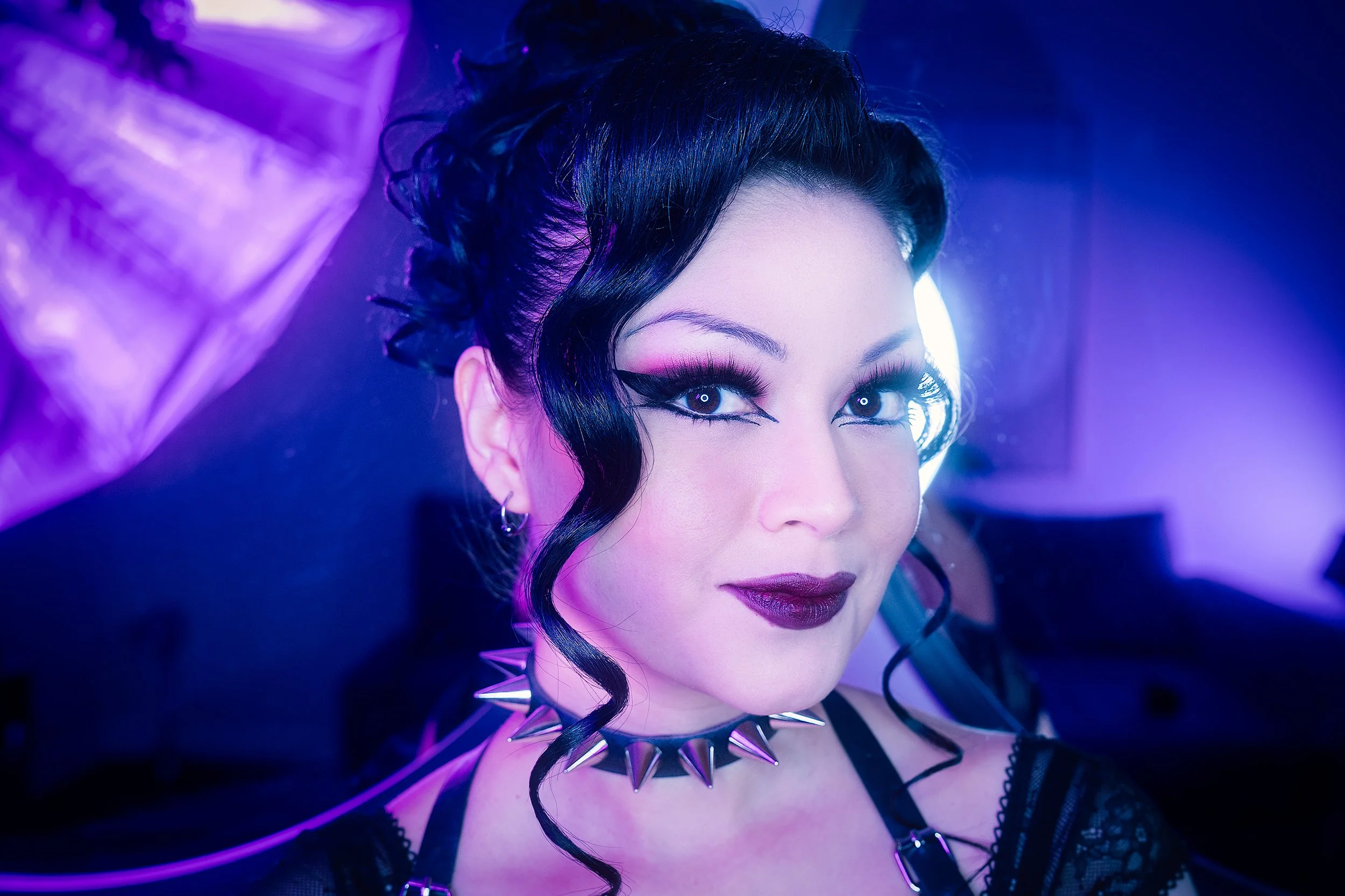 Creative studio portrait of a woman with dramatic makeup illuminated by purple and blue neon lighting.