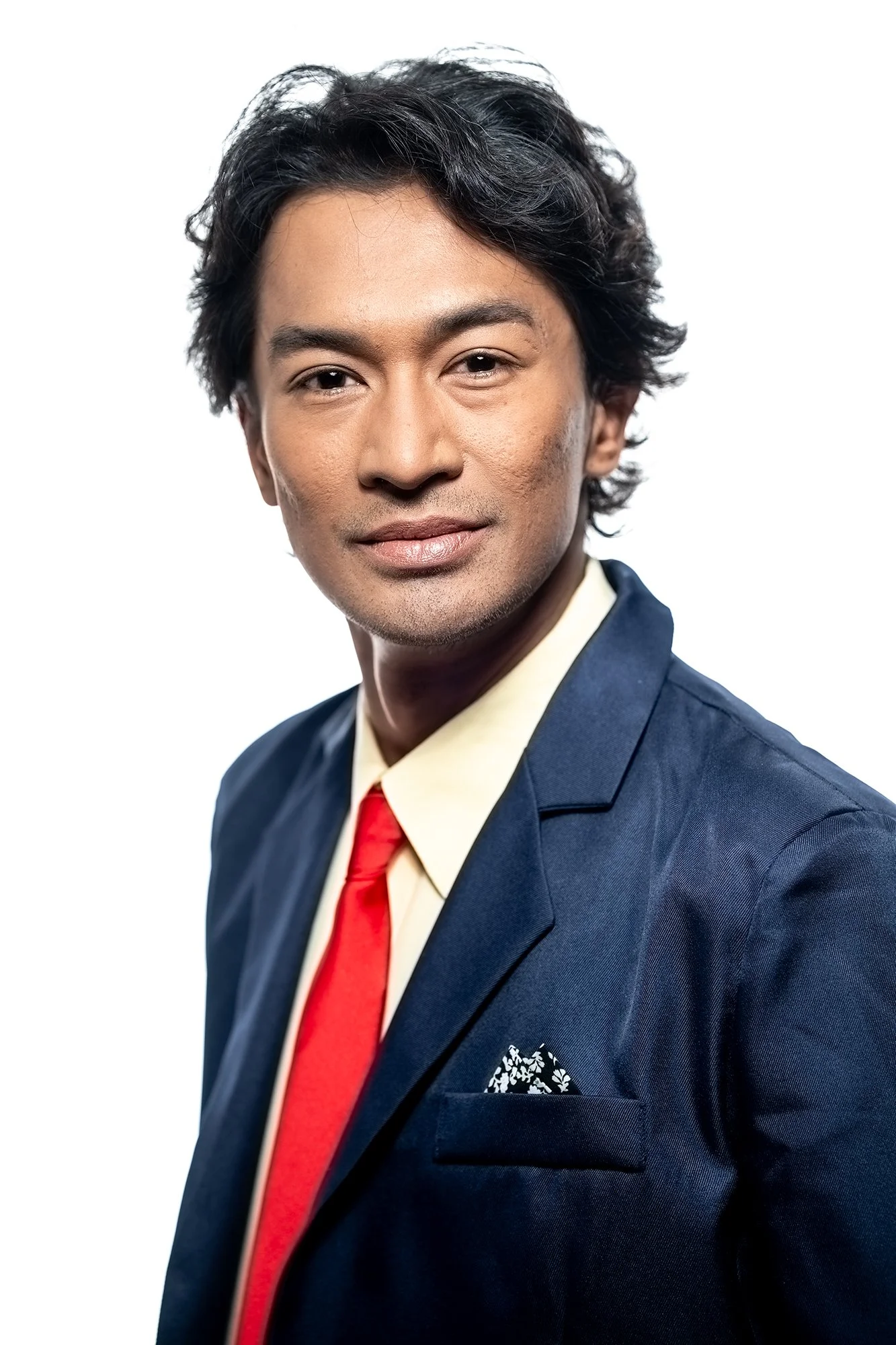 Polished business portrait of a man in a tailored suit and red tie, softly lit with a neutral background, conveying confidence and approachability.