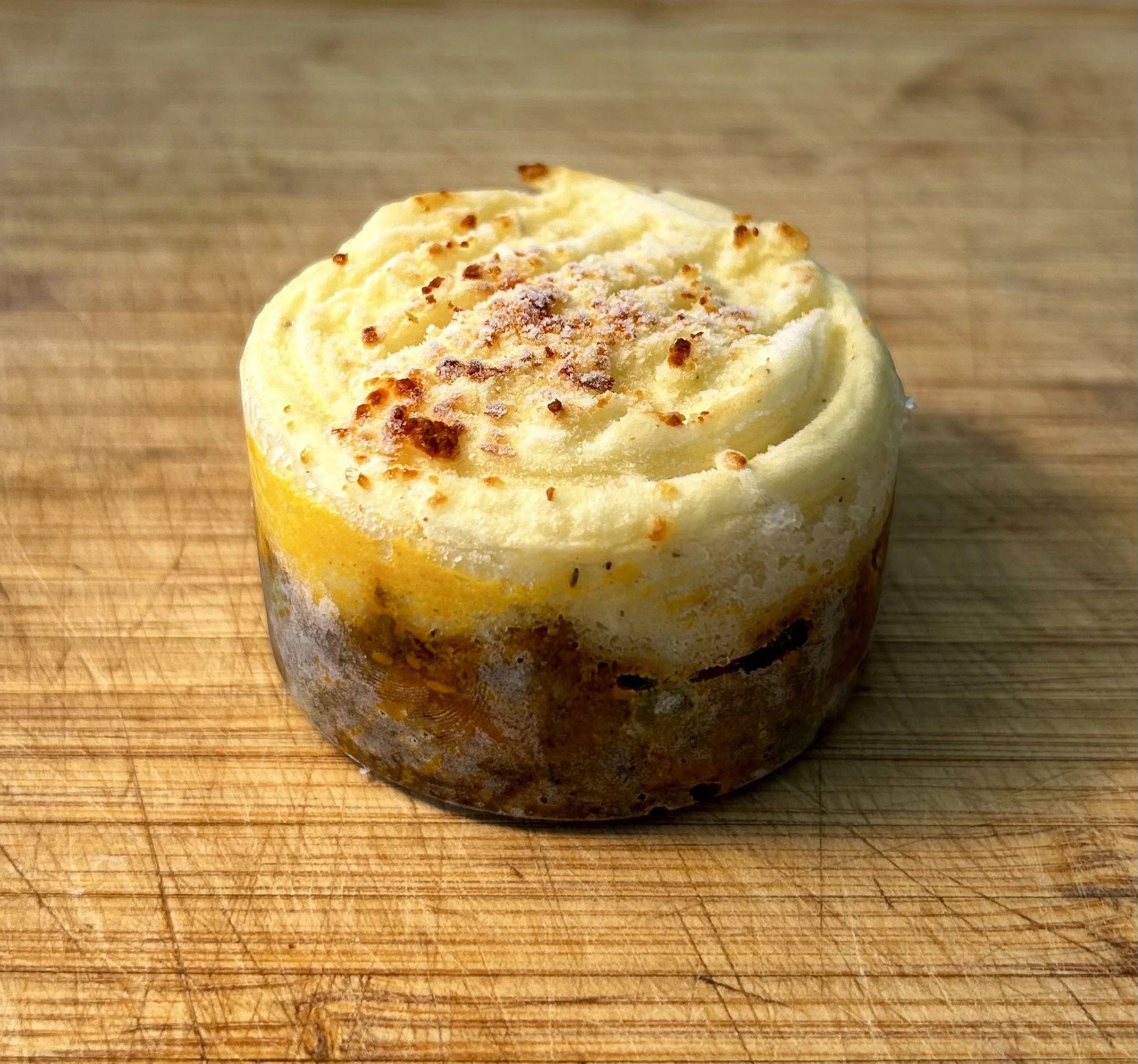 A mini sized cottage pie sitting on a wooden cutting board.