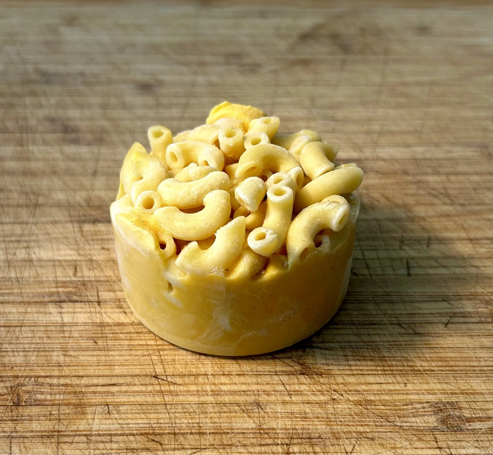 A mini childs portion of mac & cheese sitting on a wooden cutting board.