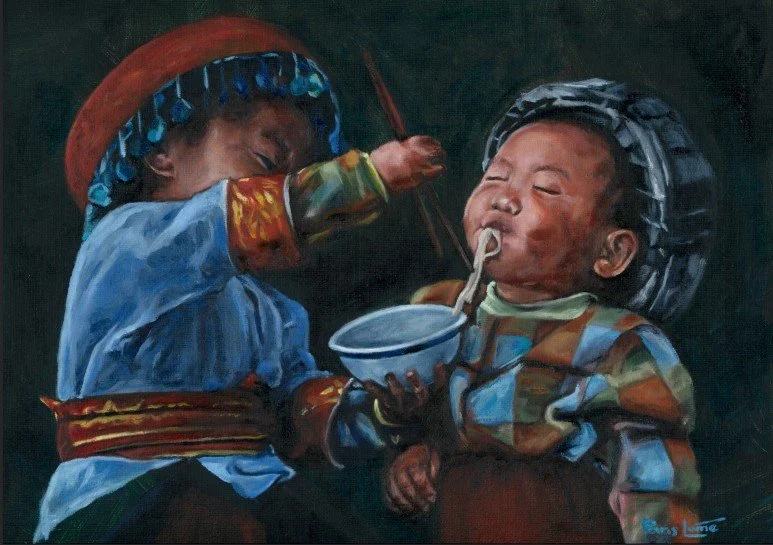 A child dressed in traditional clothing feeding a younger child who is opening his mouth to eat from a bowl with a spoon.